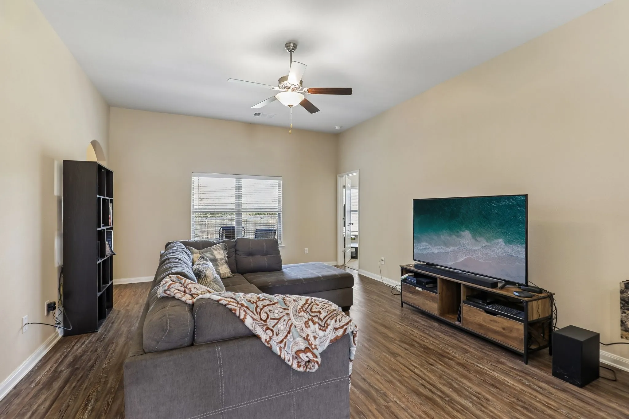 Vaulted ceiling with a ceiling fan, wood-finish flooring, and a large window with blinds