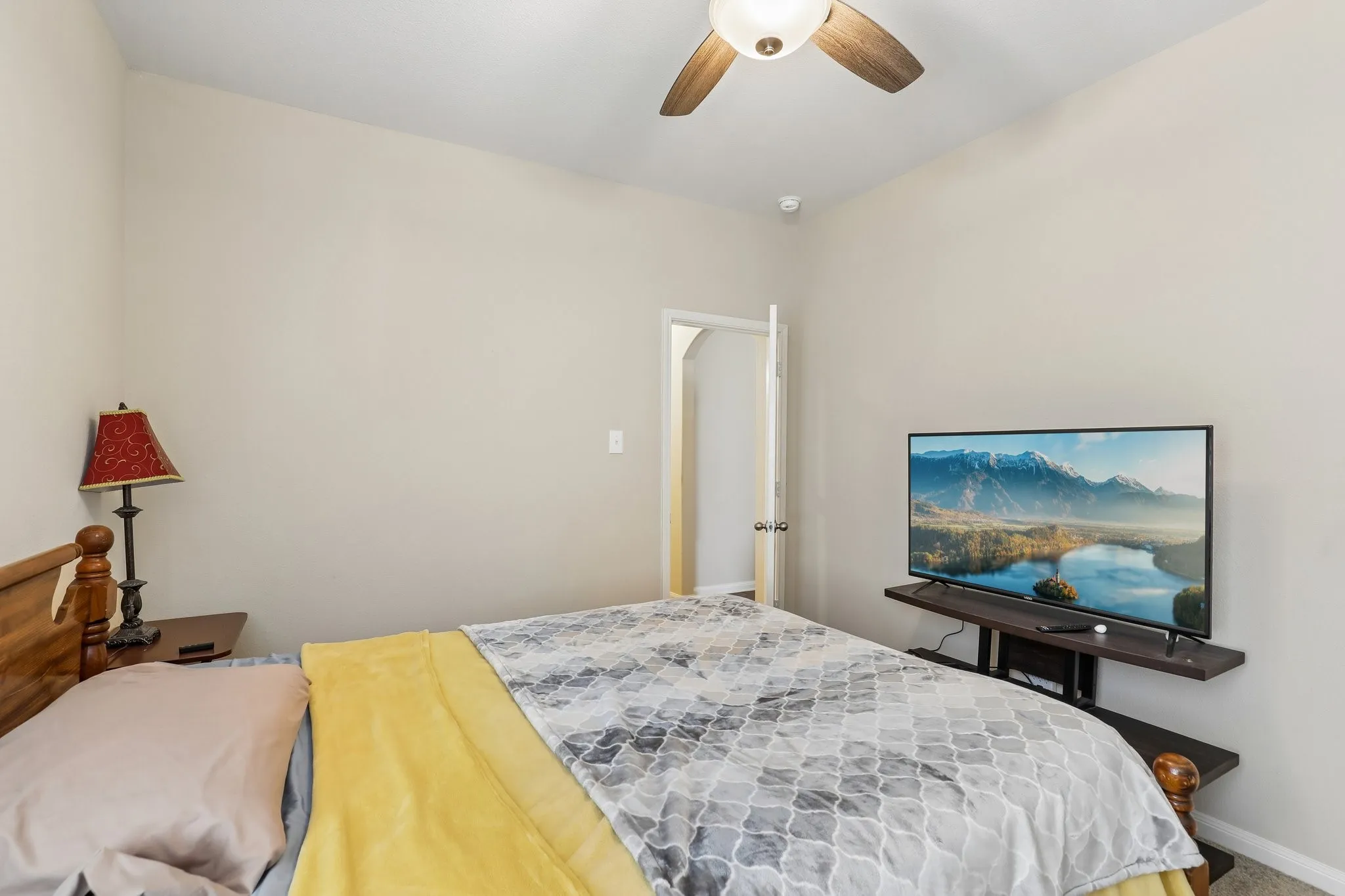 Ceiling fan with wood-finish blades, neutral wall paint, and a wall-mounted entertainment shelf