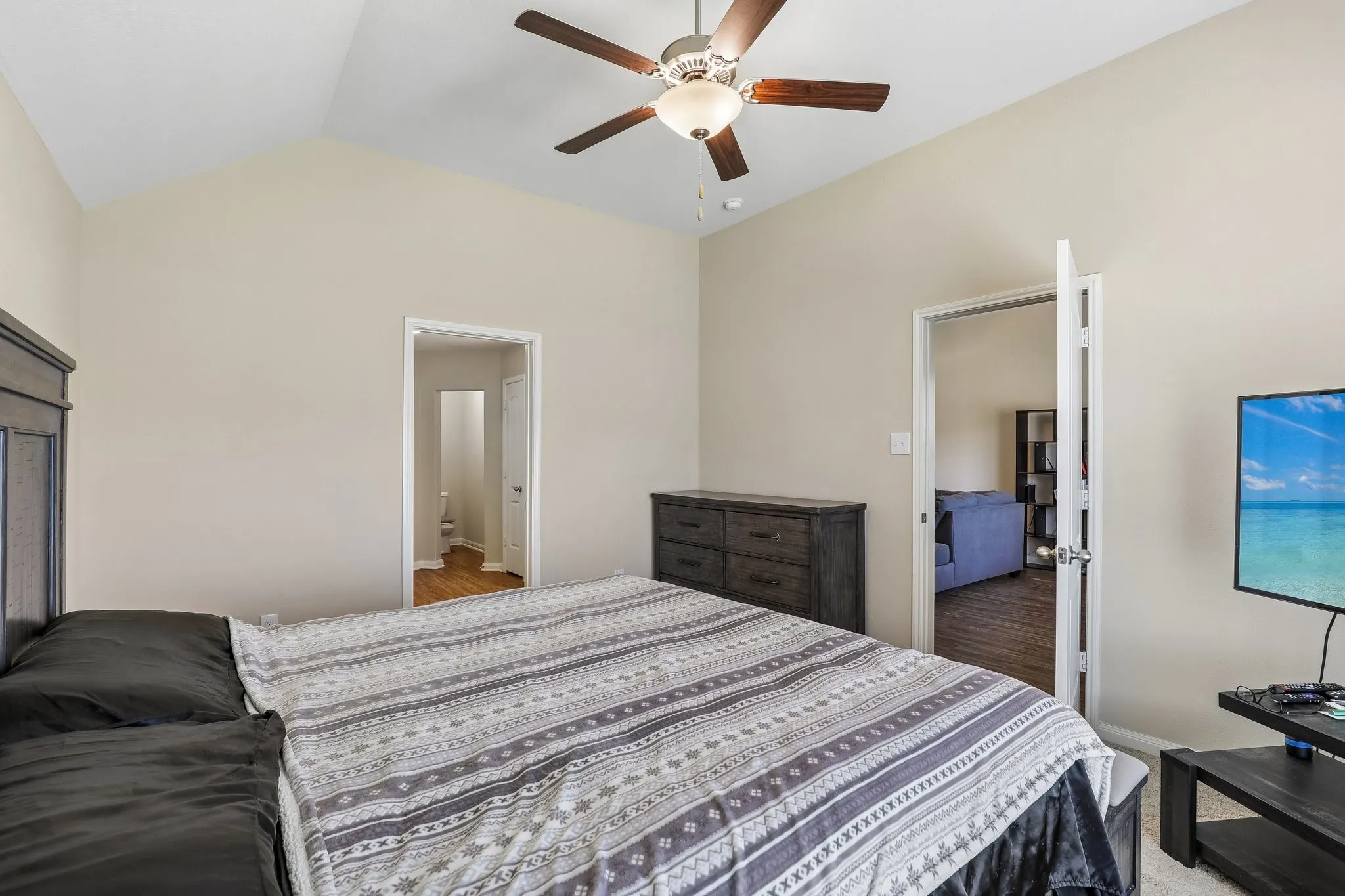 Vaulted ceiling with a ceiling fan, light neutral wall paint, and wood-finish flooring