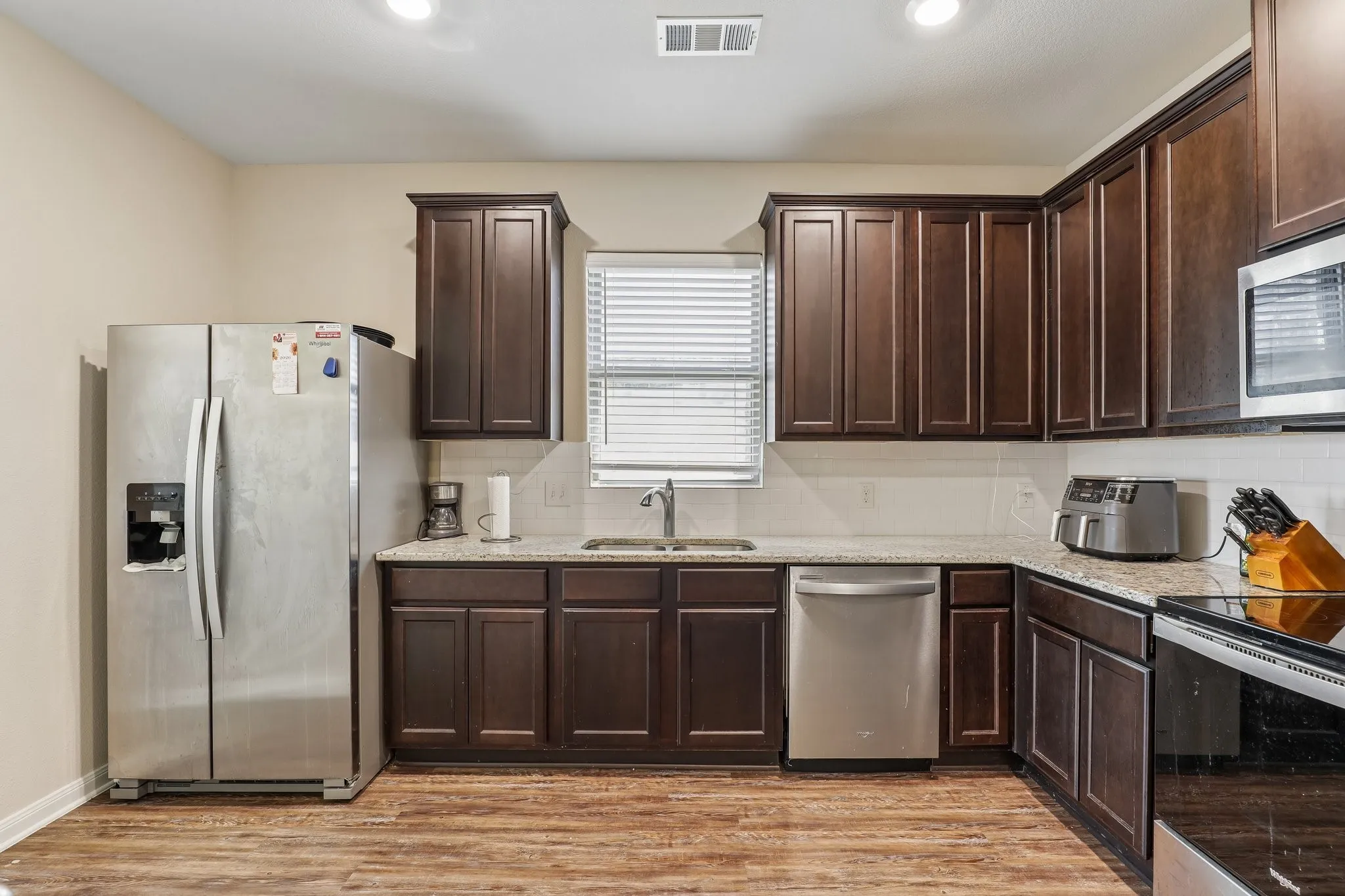 Kitchen featuring wood-finish flooring, dark wood cabinetry, light-toned countertops, and a white tile backsplash