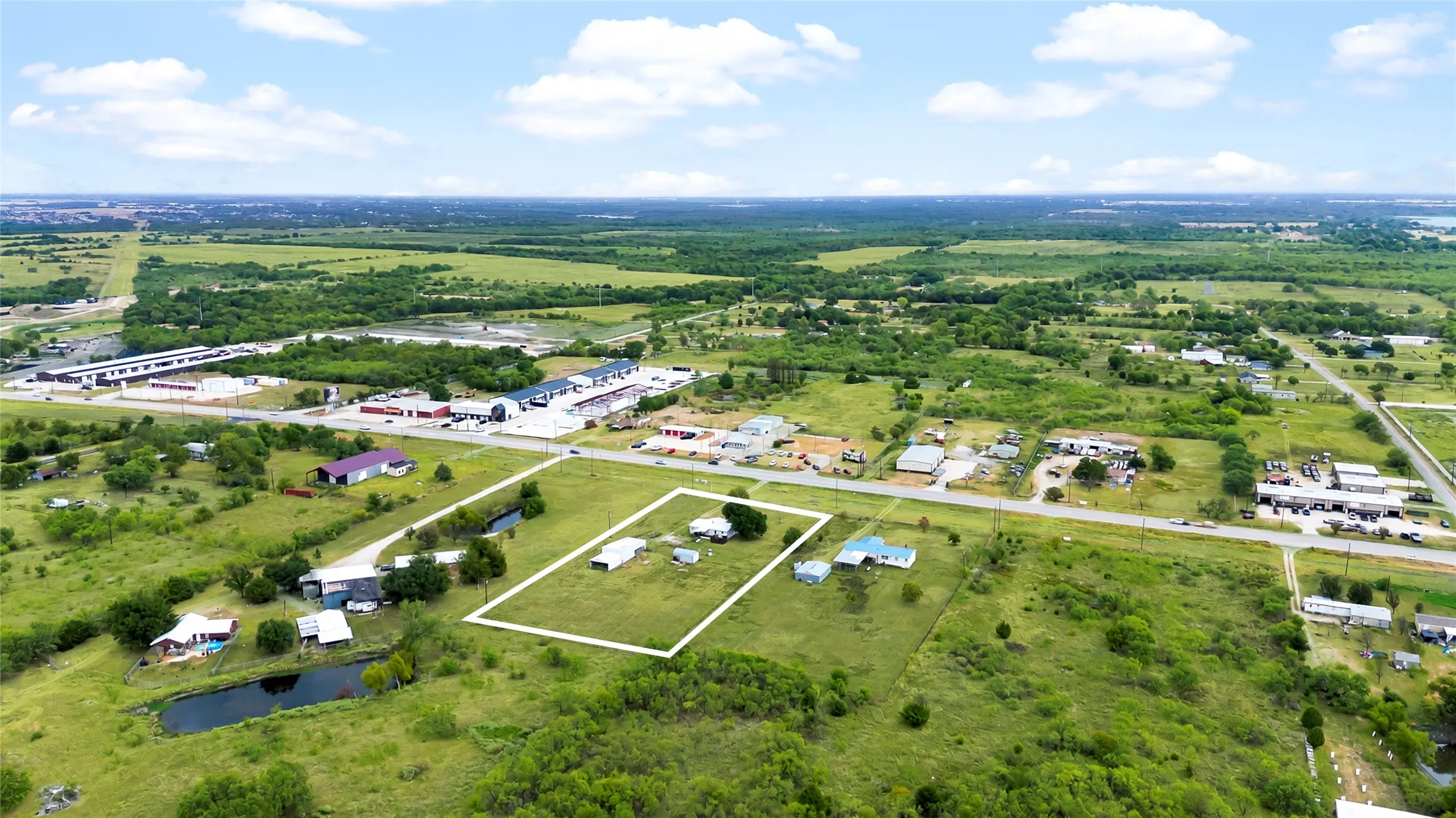 Expansive green land area with multiple structures, direct road frontage, and a defined property boundary