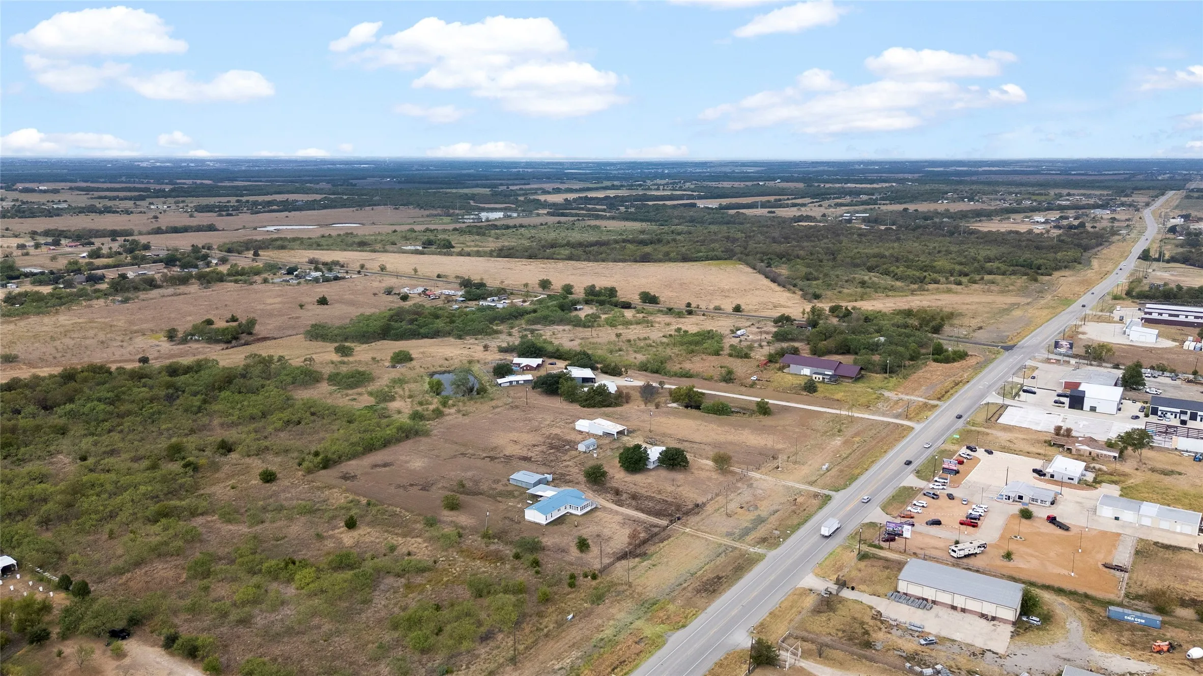 Expansive land parcel featuring a visible roadway, scattered structures, and an overall rural setting