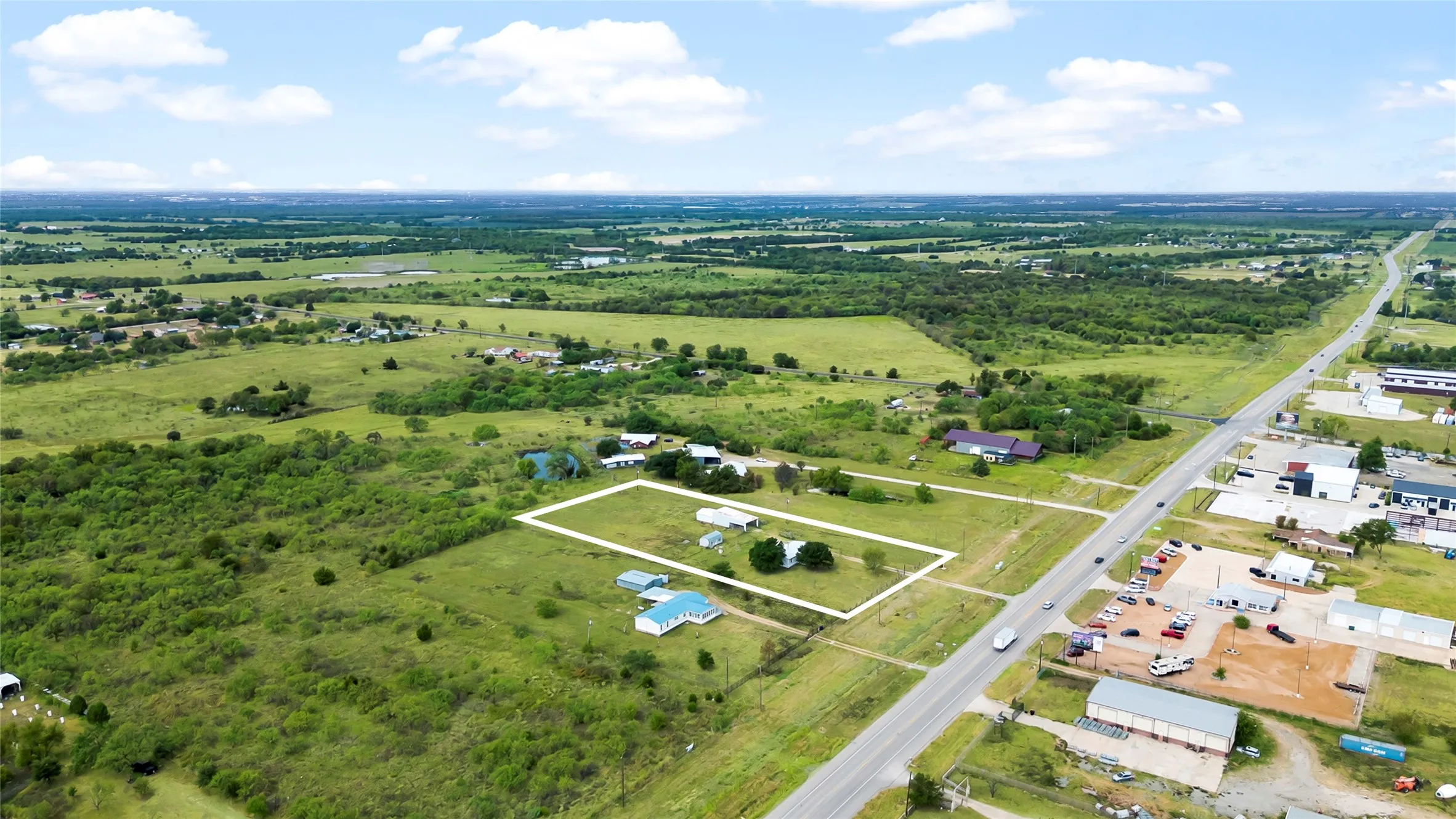 Expansive rural property with existing structures, bordered by a paved roadway