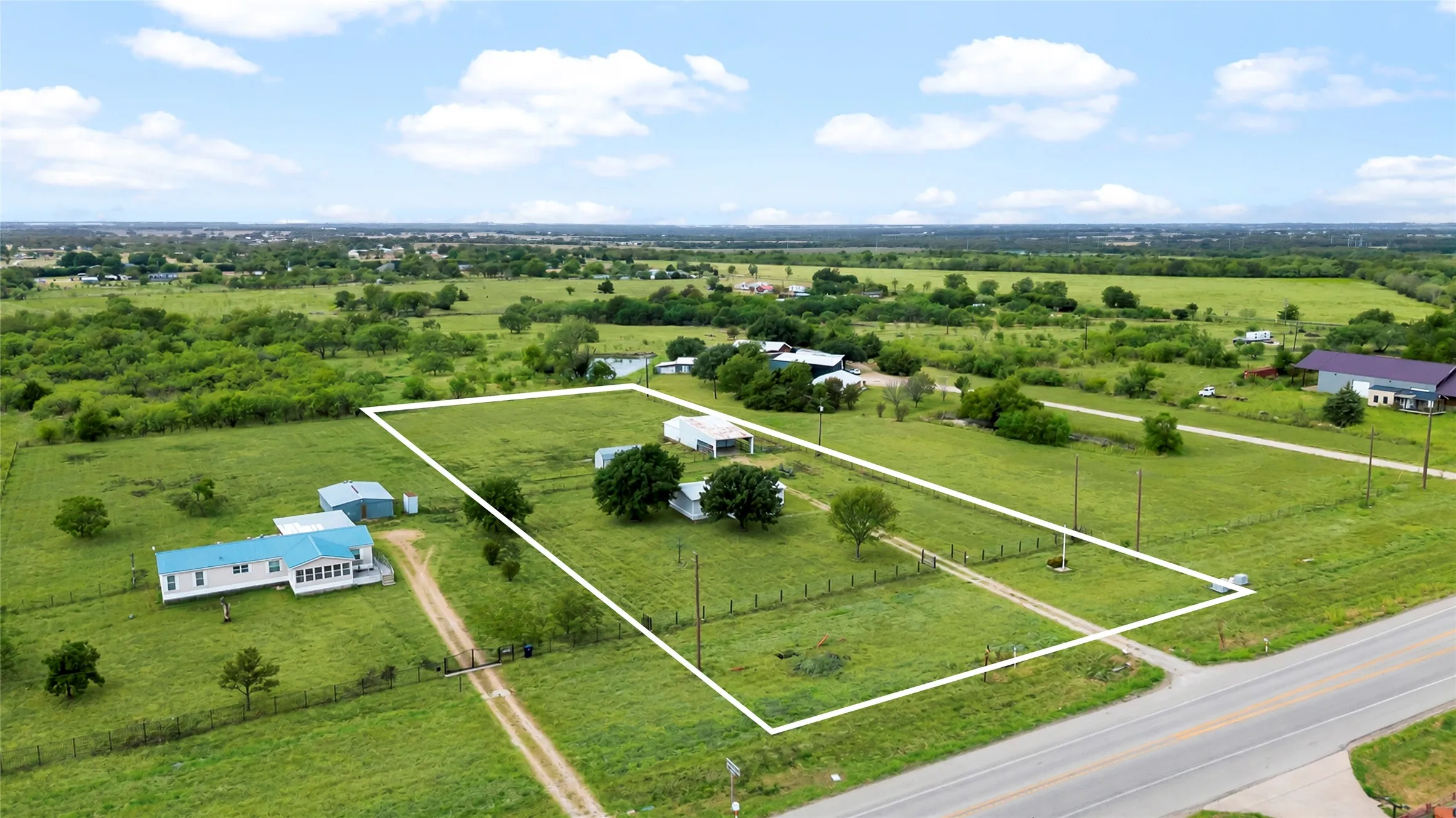 Expansive green acreage with a distinct boundary, multiple outbuildings, mature trees, and direct road access
