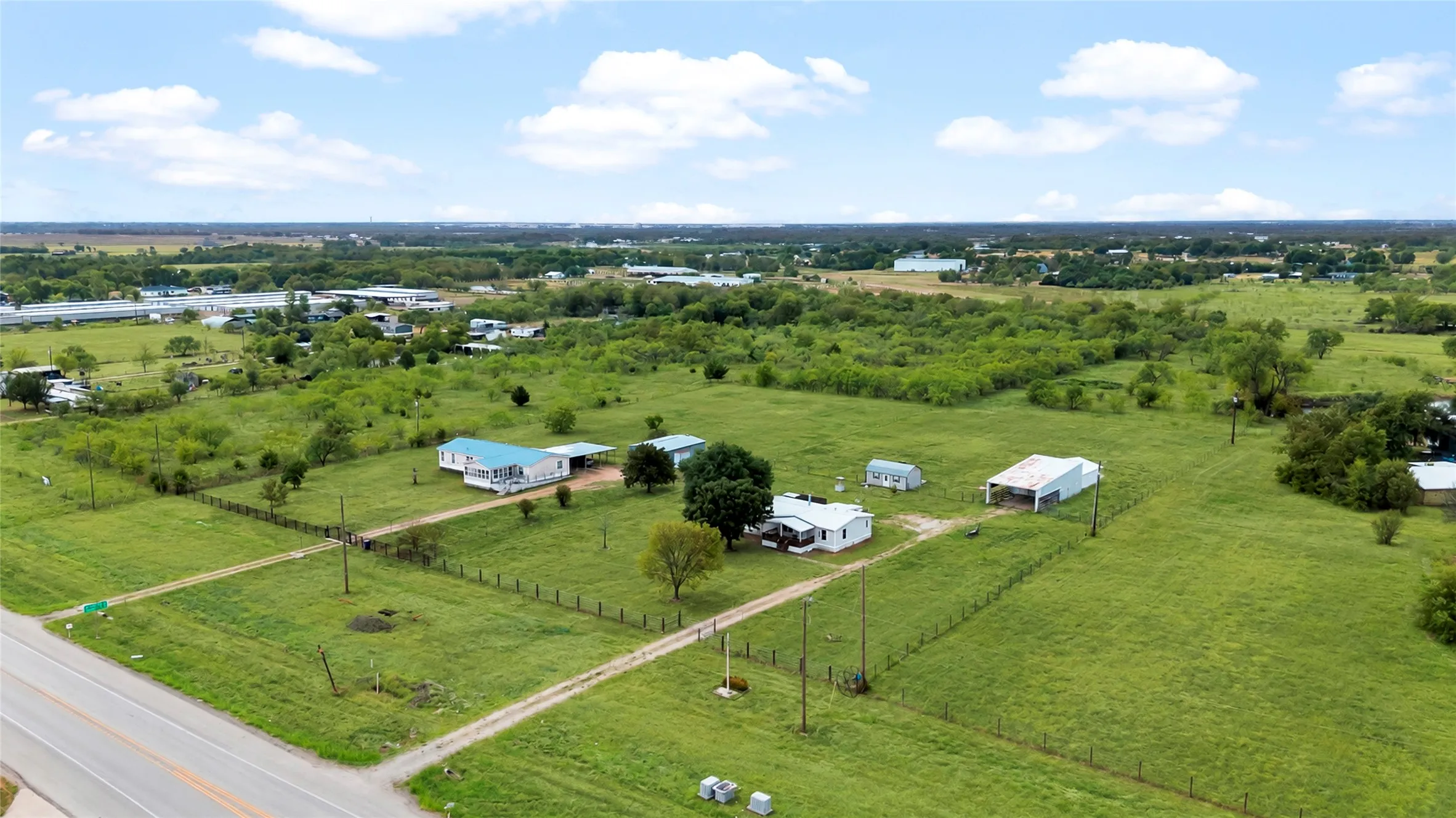 Expansive green landscape with multiple buildings, including a residence with a blue roof, a white residence, and a large outbuilding