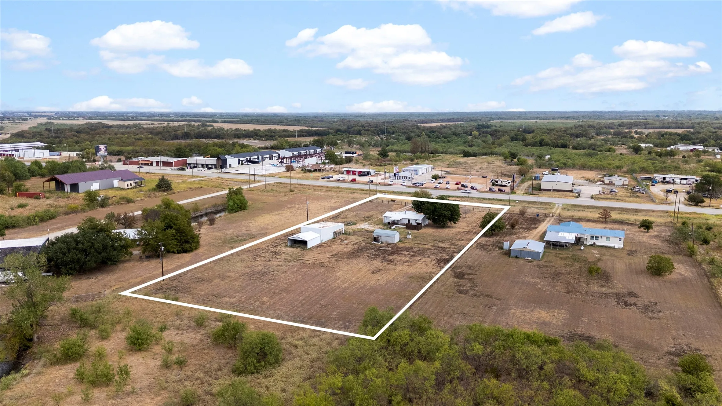 Expansive lot with cleared land, a single-story residence, and multiple outbuildings