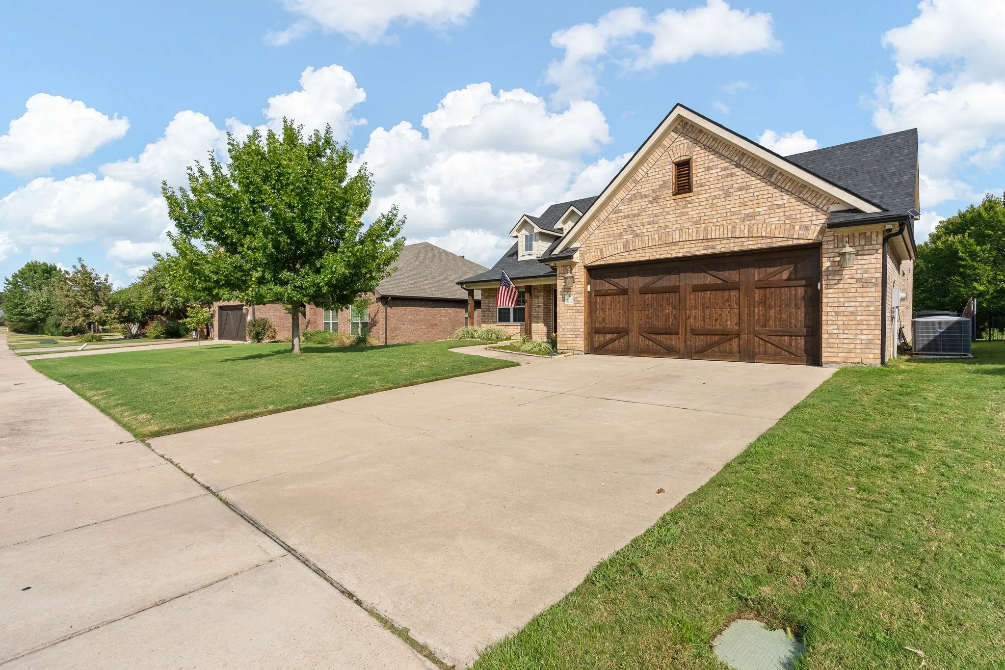 Brick exterior with dormer windows, dark shingle roof, and wood-finish garage doors