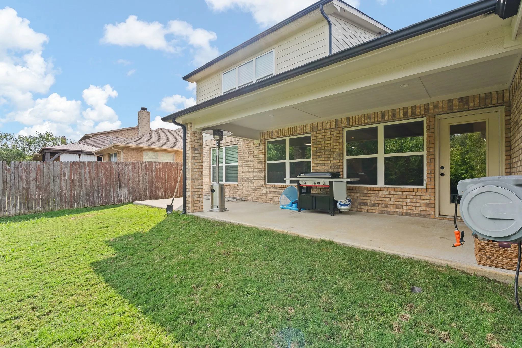 Covered patio with concrete flooring, brick column, and wood privacy fencing