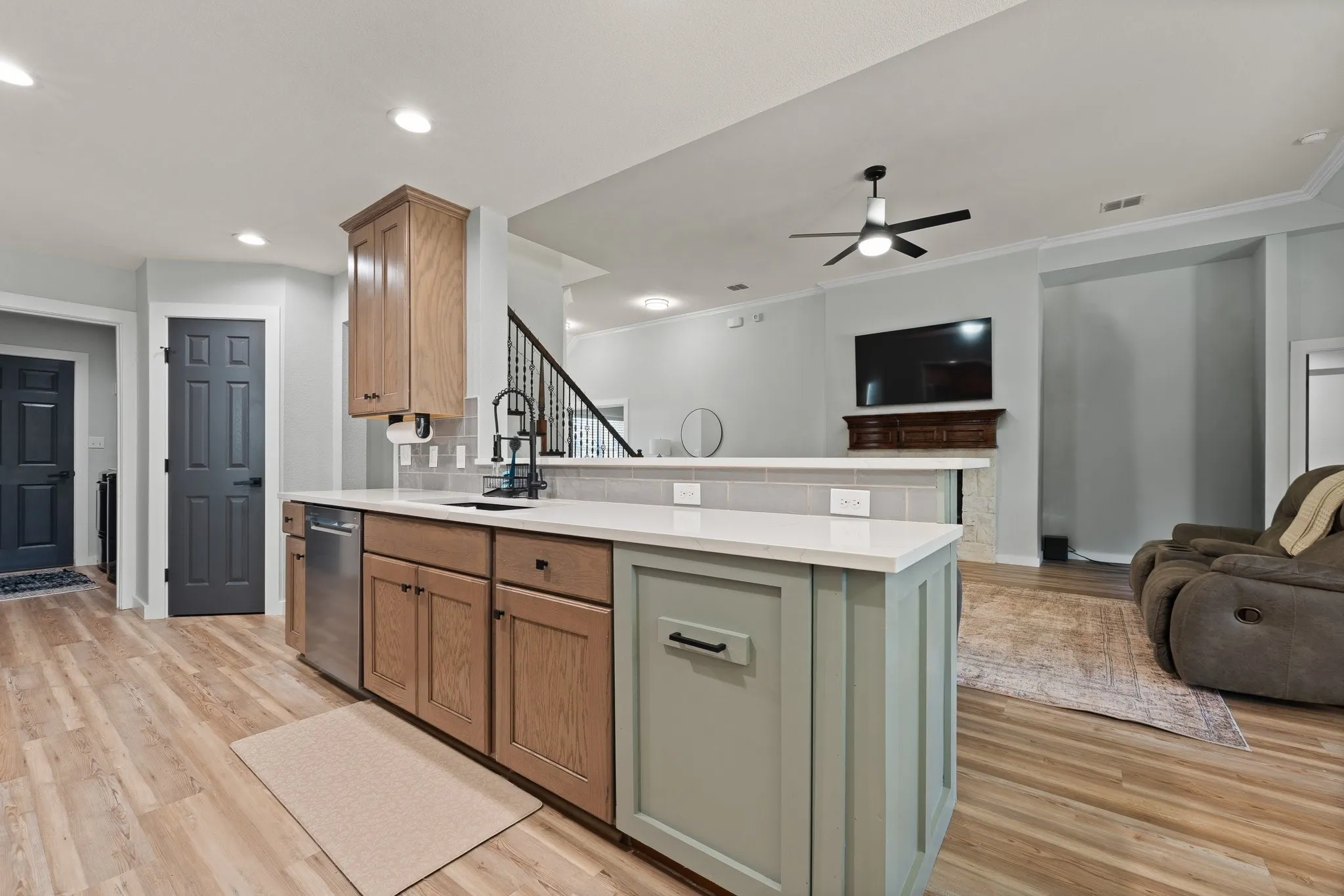 Open-concept kitchen and living area featuring custom cabinetry with mixed wood and painted finishes, white quartz countertops, stainless steel appliances, wood-finish flooring throughout, and ceiling fan with recessed lighting