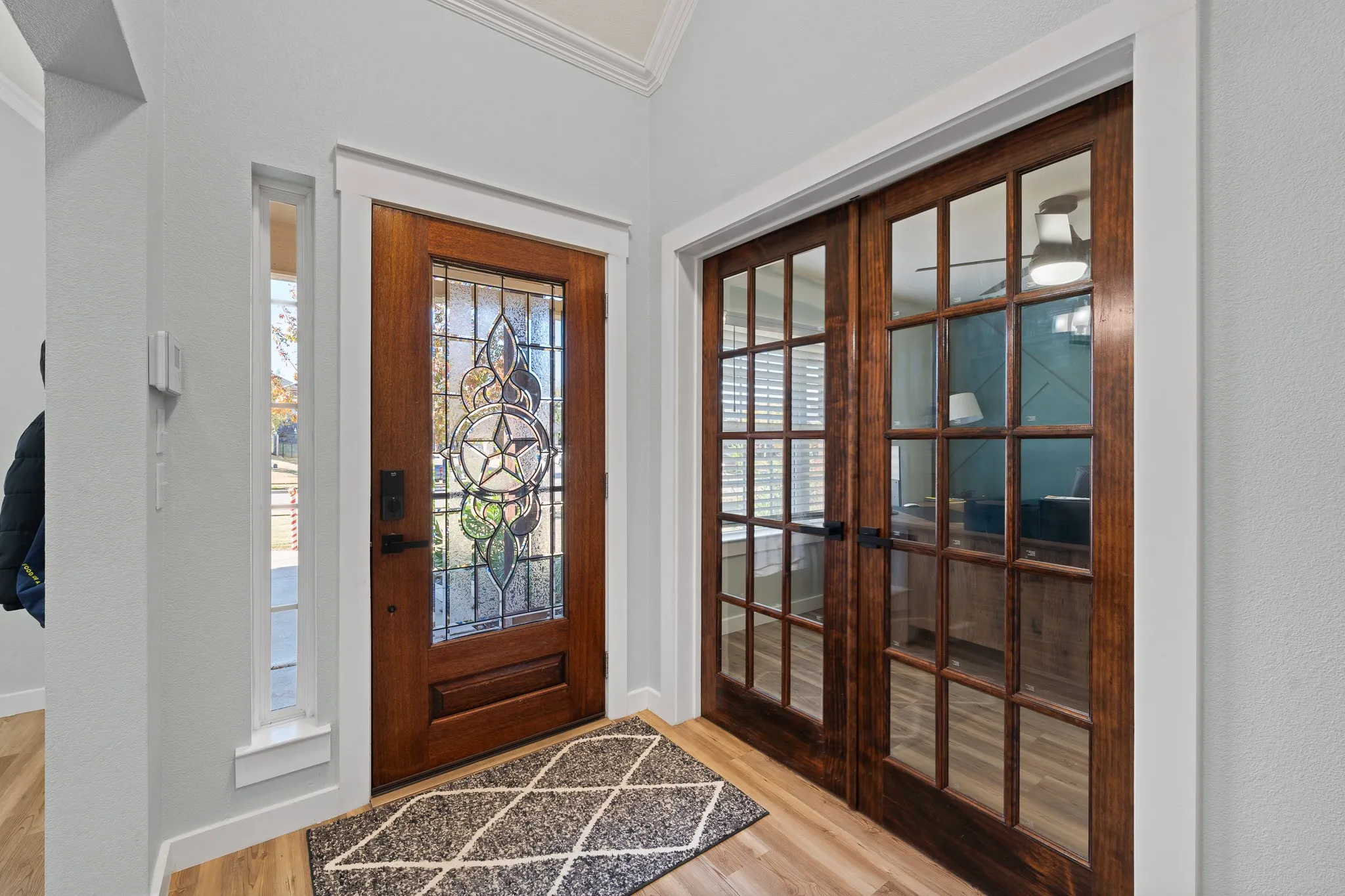 Wood-finish flooring, accent wall with geometric paneling, ceiling fan with integrated lighting, dual pane window with blinds, and paneled bifold doors