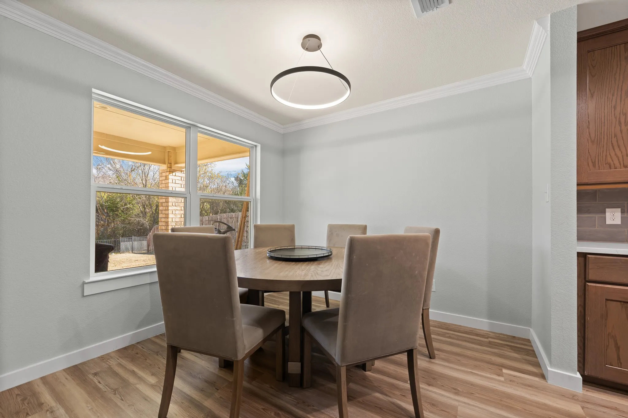 Wood-finish flooring throughout, complemented by a contemporary circular light fixture, stainless steel appliances, wood cabinetry, and a tile backsplash