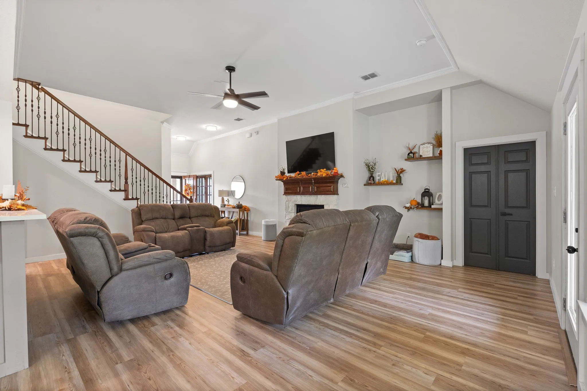Wood-finish flooring, staircase with dark wood handrail and metal spindles, vaulted ceiling, fireplace with wood mantel, and built-in shelving