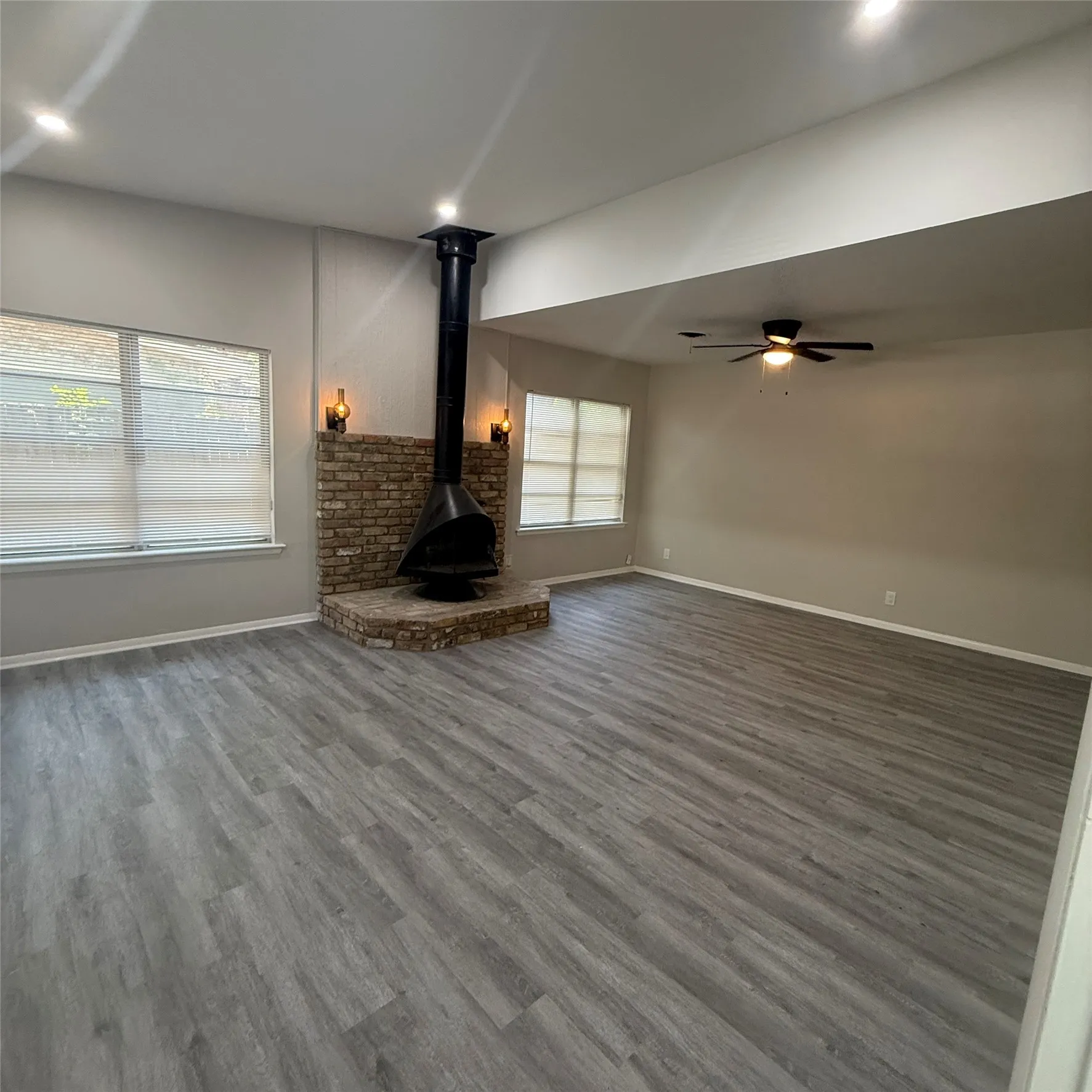 Vaulted ceiling with recessed lighting, wood-finish flooring, brick-faced fireplace with a suspended metal firebox, ceiling fan, and multiple windows
