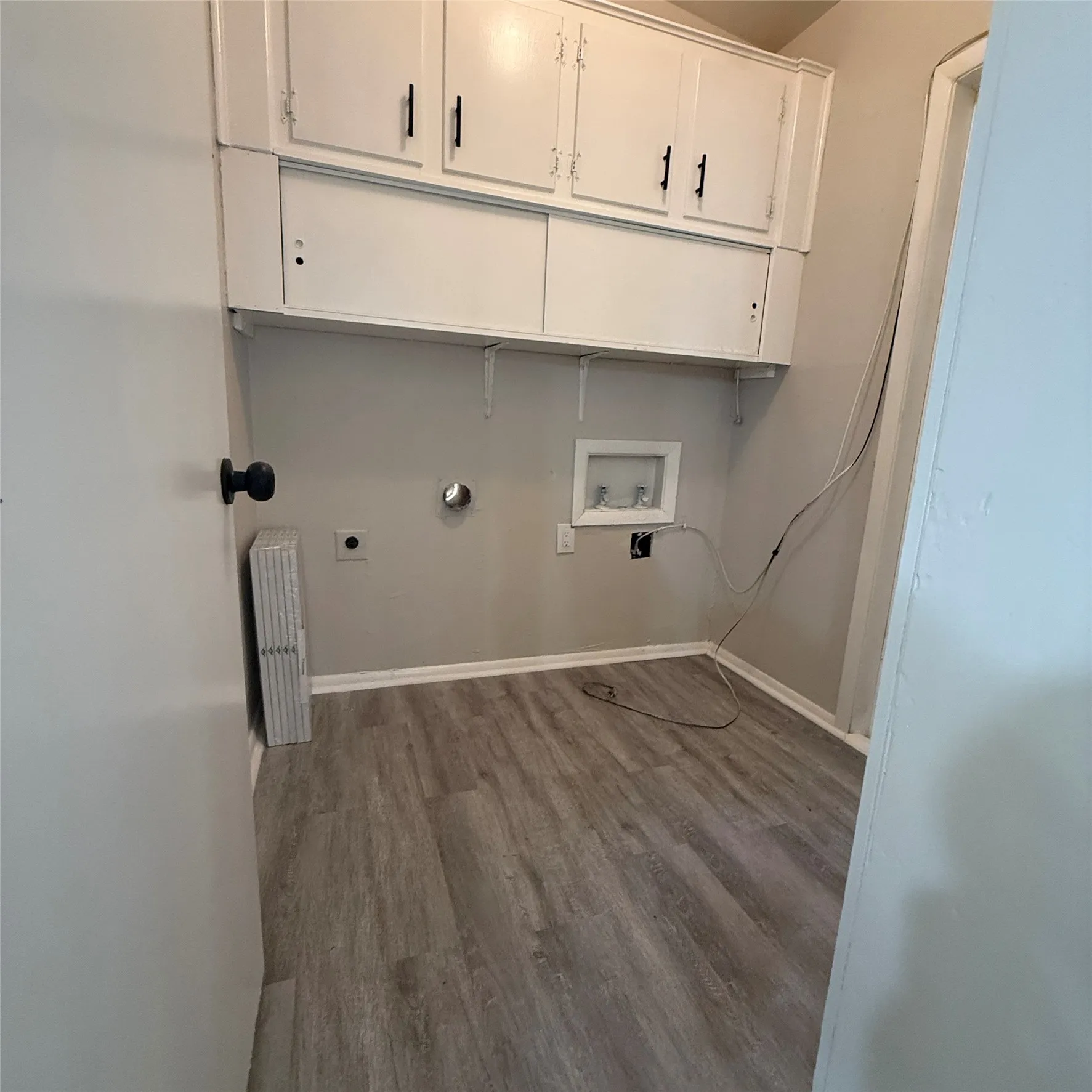 Laundry area featuring wood-finish flooring, white wall cabinets, and light gray wall paint