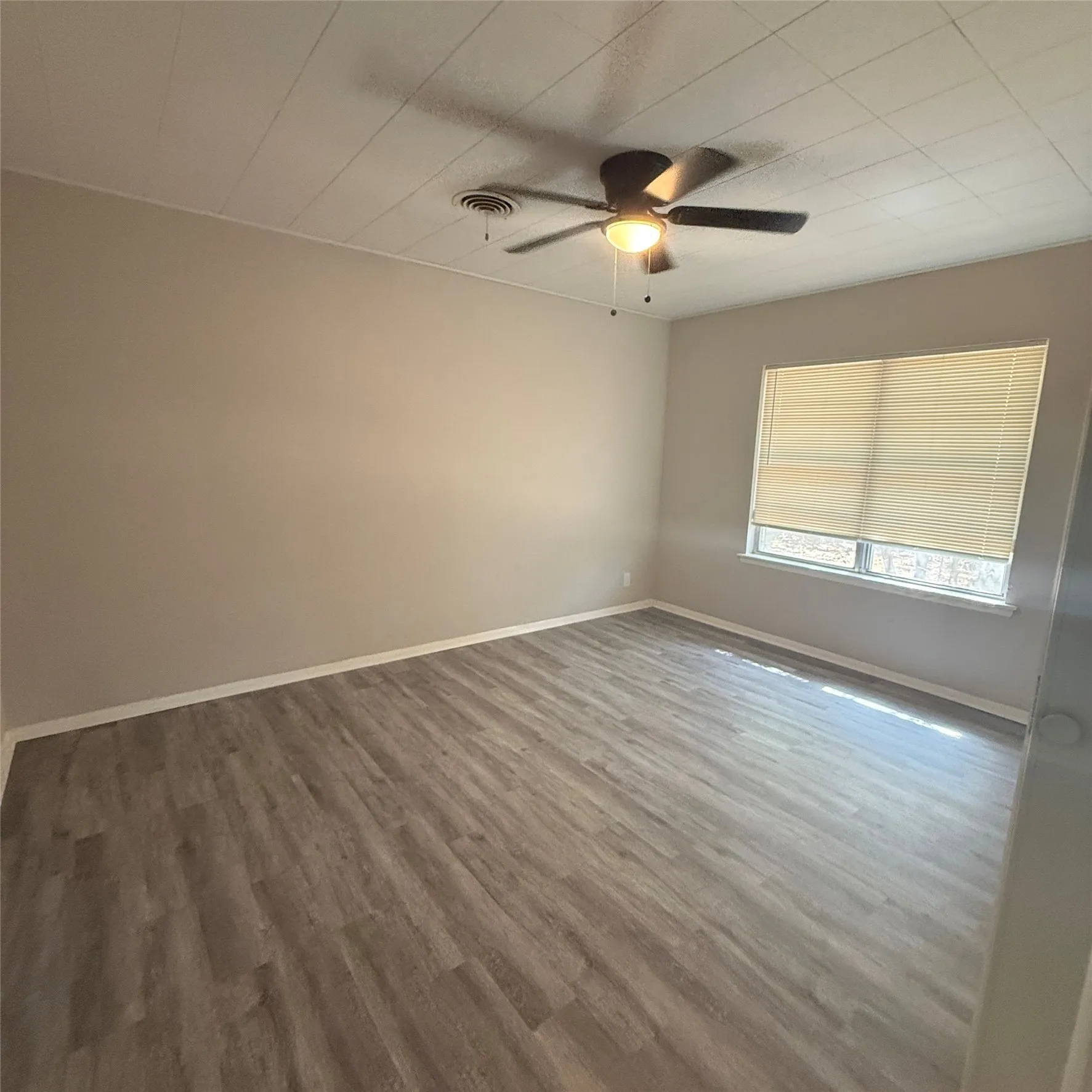 Neutral tone paint throughout, wood-finish flooring, ceiling fan with integrated lighting, and a window with blinds