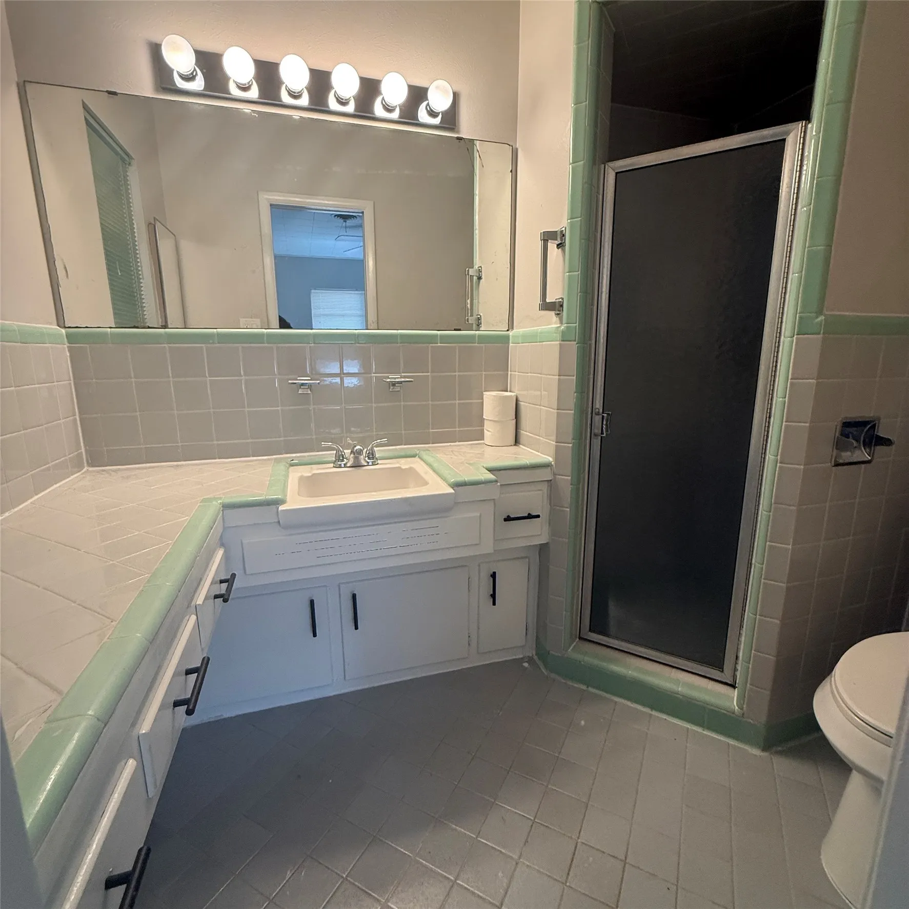 Bathroom featuring a built-in vanity with an integrated sink, a shower enclosure with a frosted glass door, tile flooring, and a large wall-mounted mirror with overhead lighting