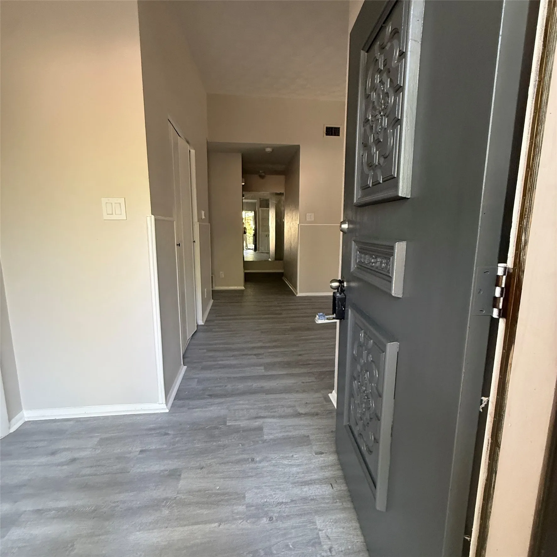 Detailed decorative entry door with dark finish, gray wood-finish flooring throughout, and light neutral wall colors