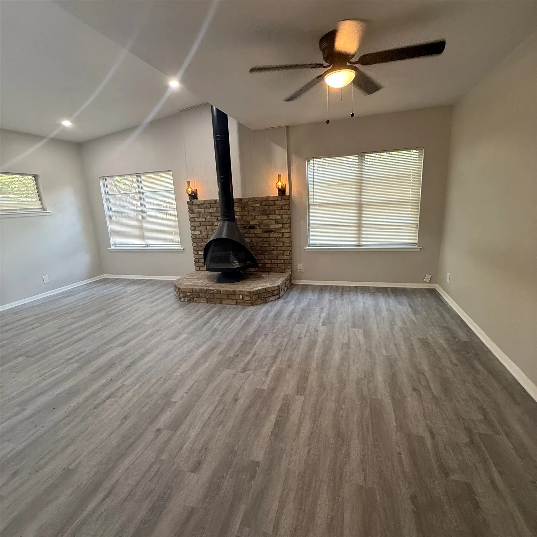 Vaulted ceiling, recessed lighting, wood-finish flooring, brick fireplace with a suspended firebox, and a ceiling fan