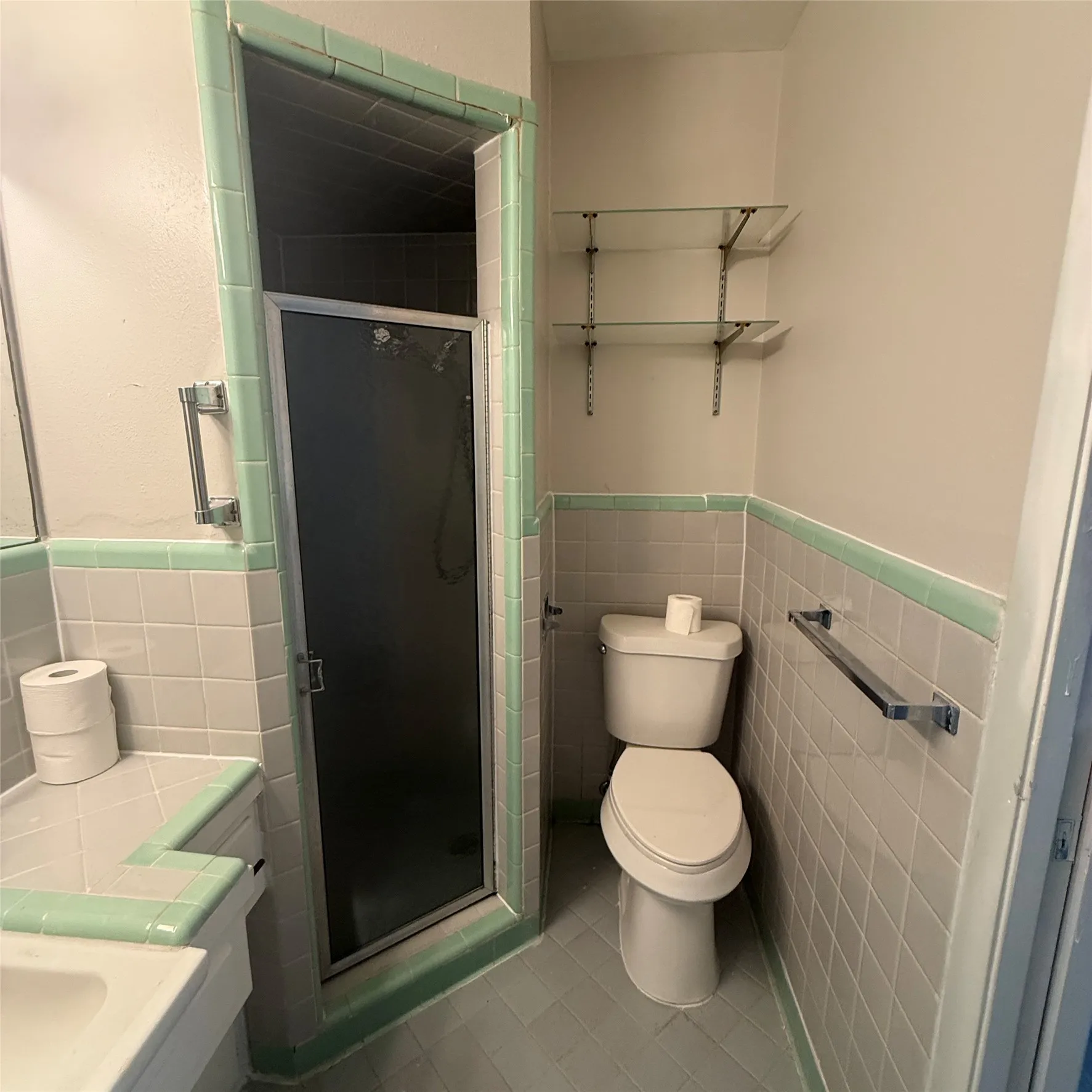 Tiled bathroom featuring a glass-enclosed shower, wall-mounted shelving, and a toilet
