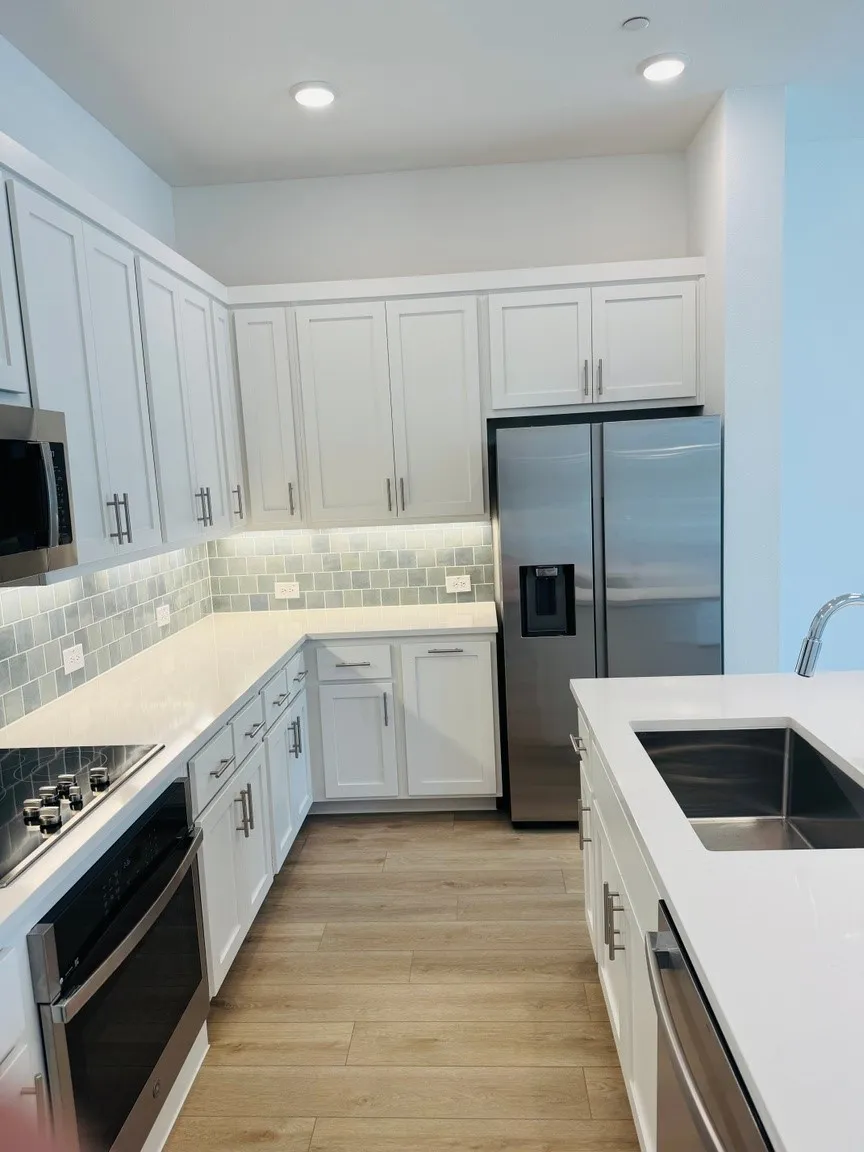 White shaker cabinetry, stainless steel appliances, light-toned wood-finish flooring, undermount sink, and recessed lighting