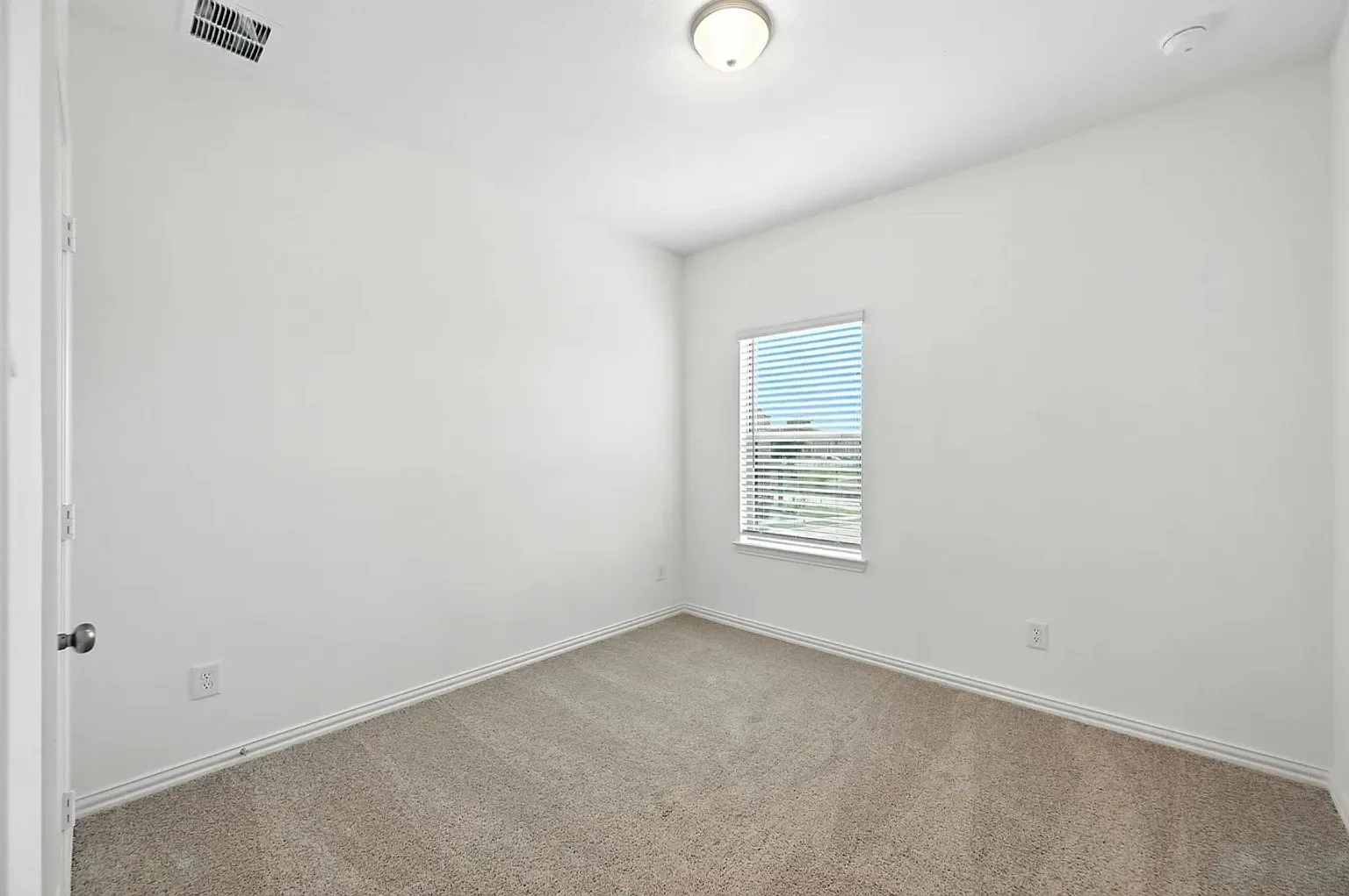 Neutral wall paint, carpet flooring, a single window with blinds, and a flush mount ceiling light fixture
