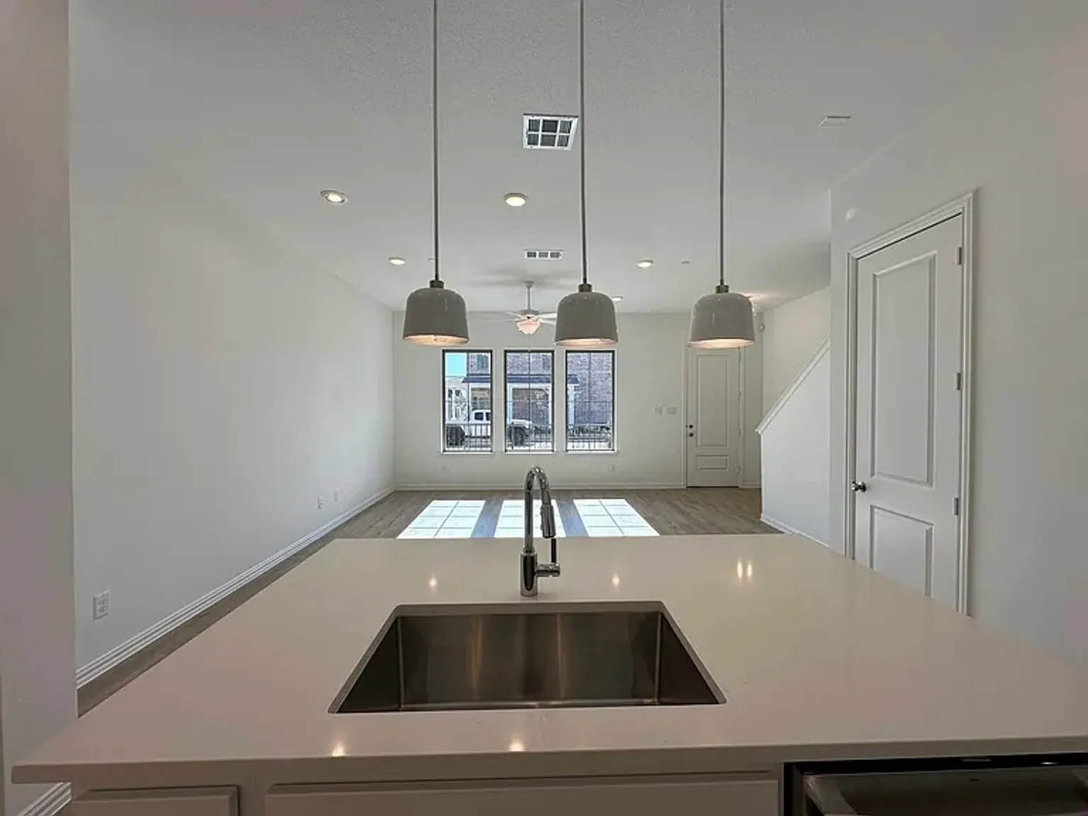 Kitchen island with an undermount stainless steel sink, contemporary pendant lighting, wood-finish flooring, recessed ceiling lighting, and a built-in dishwasher