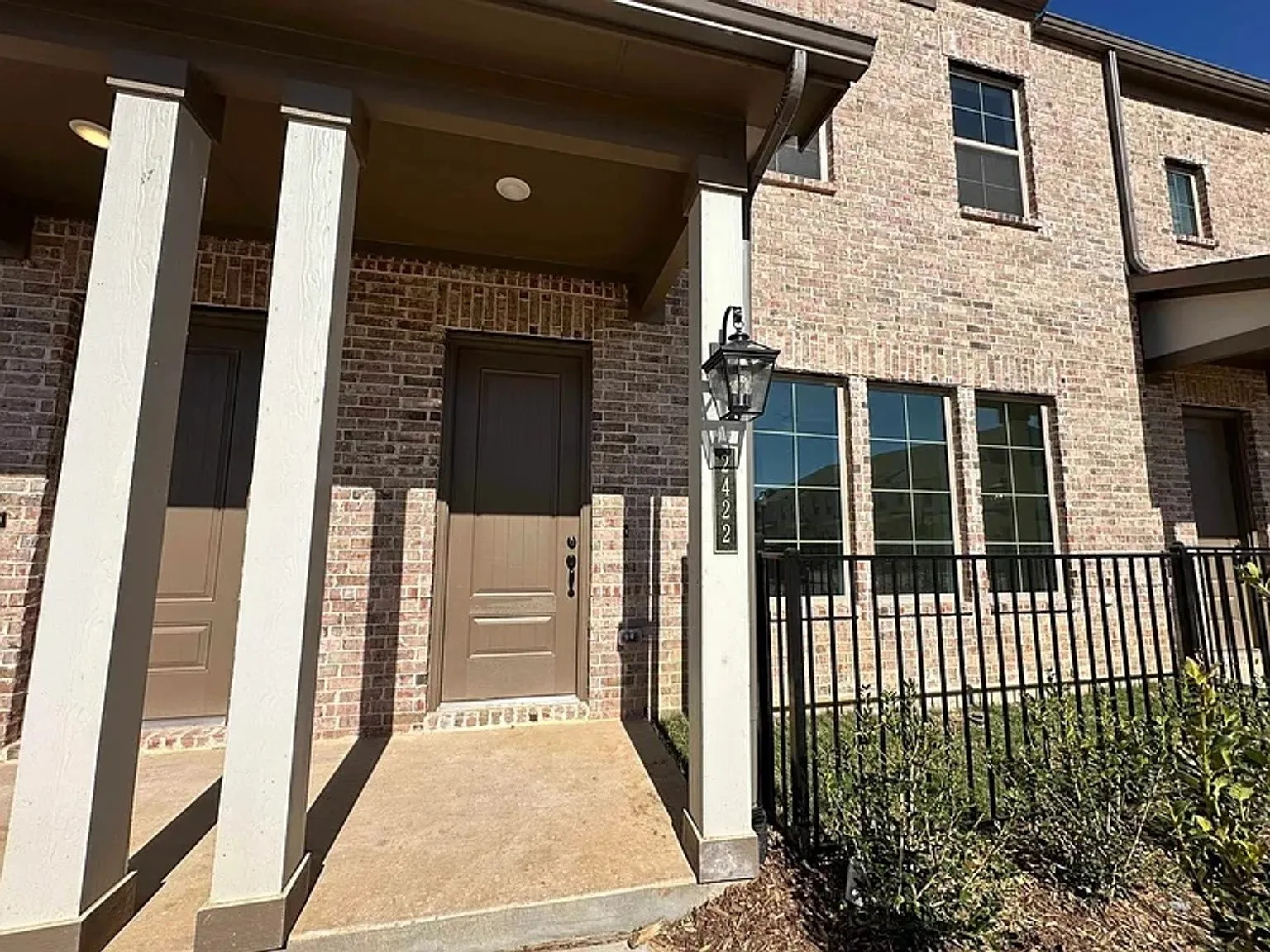 Brick facade with a covered entry, dark paneled entry door, black wrought iron fencing, and multi-pane windows