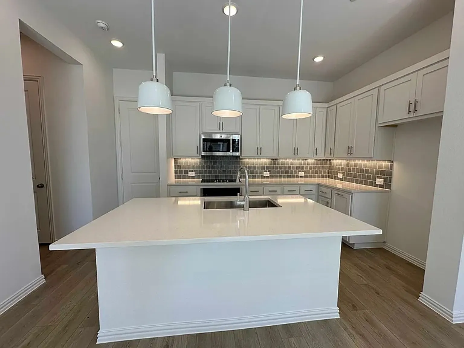 Kitchen featuring a large central island with a built-in sink, stainless steel appliances, white cabinetry, and wood-finish flooring