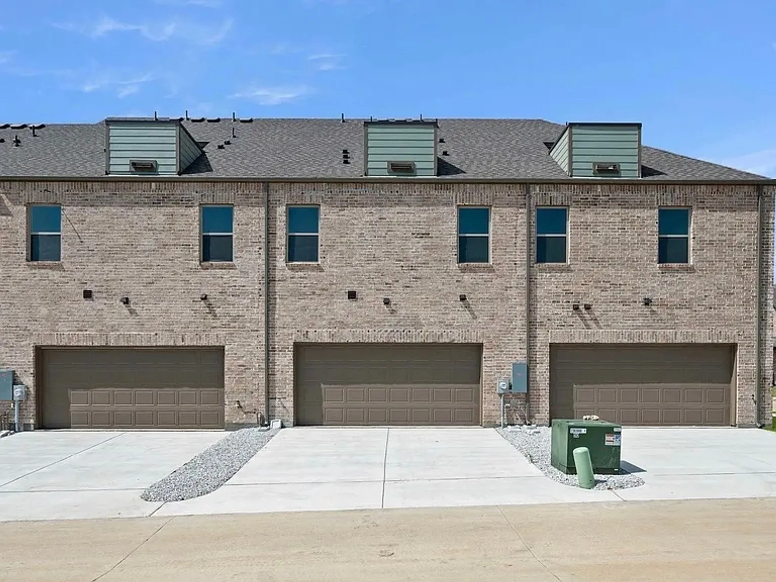 Brick exterior with multiple dormer windows, individual garage doors, and concrete driveways