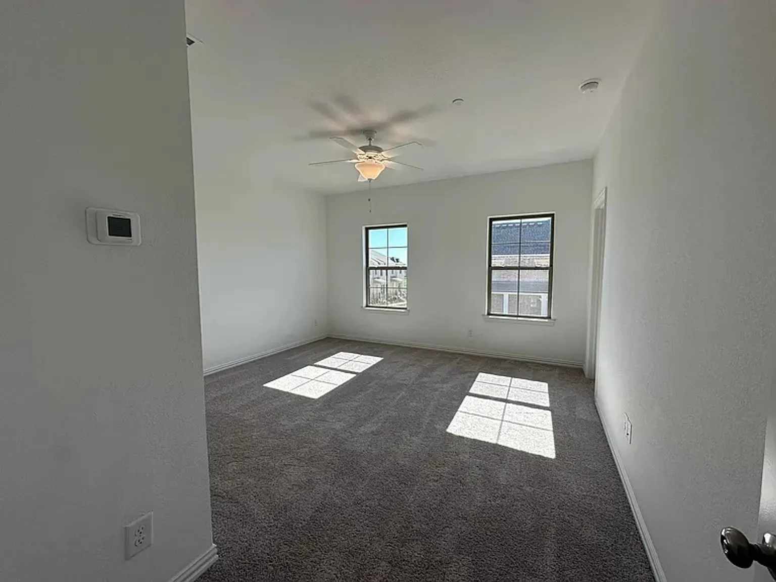 Spacious room featuring neutral carpeting, two large windows, a ceiling fan with integrated lighting, and a recessed light fixture