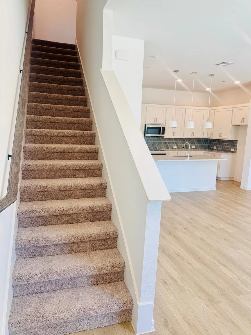Carpeted staircase with contemporary railing, light wood-finish flooring, white cabinetry, integrated microwave, and pendant lighting
