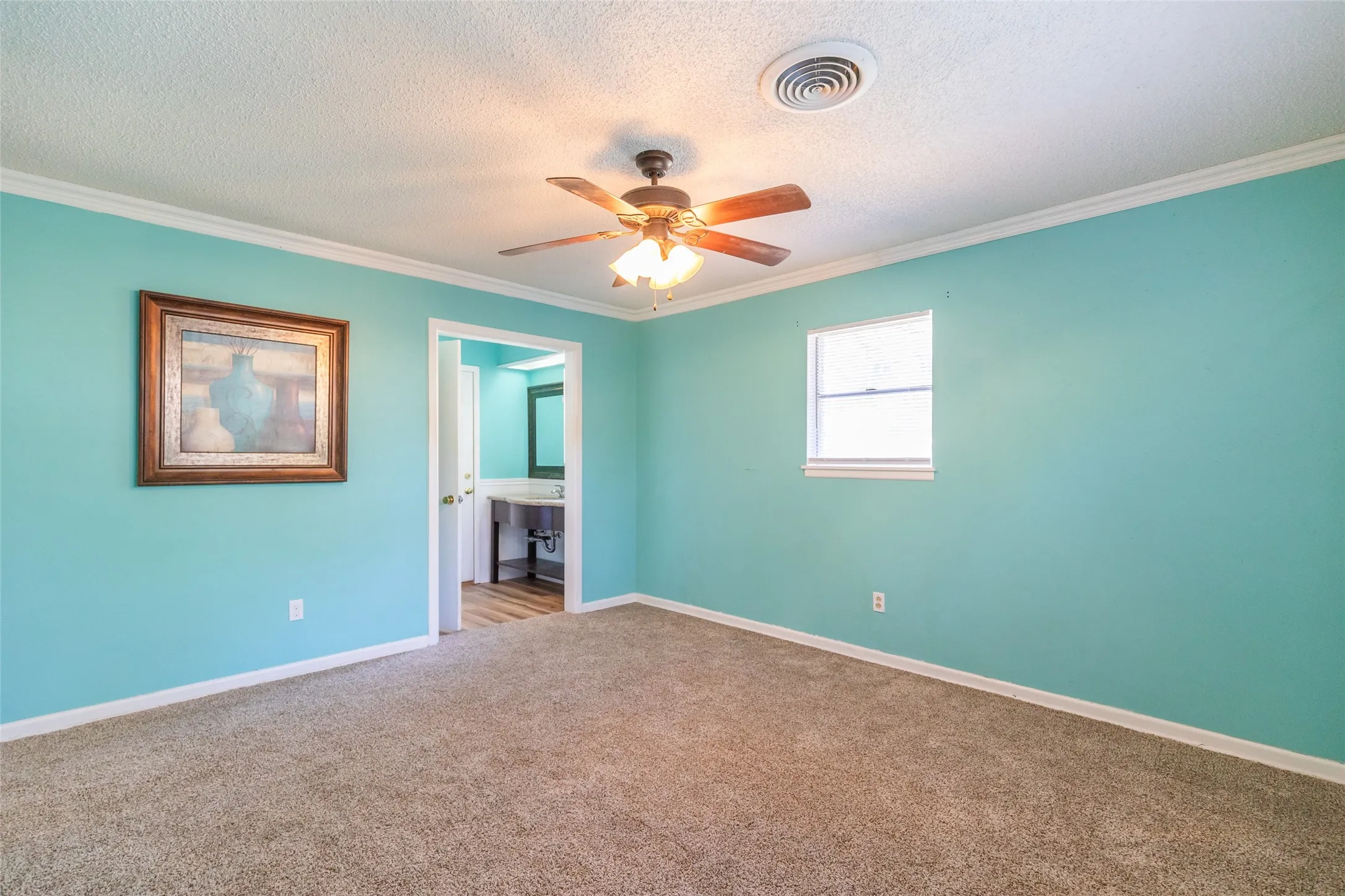 Carpeted flooring, ceiling fan with integrated lighting, single window, and a doorway opening to an additional space featuring wood-finish flooring and a vanity with an integrated sink
