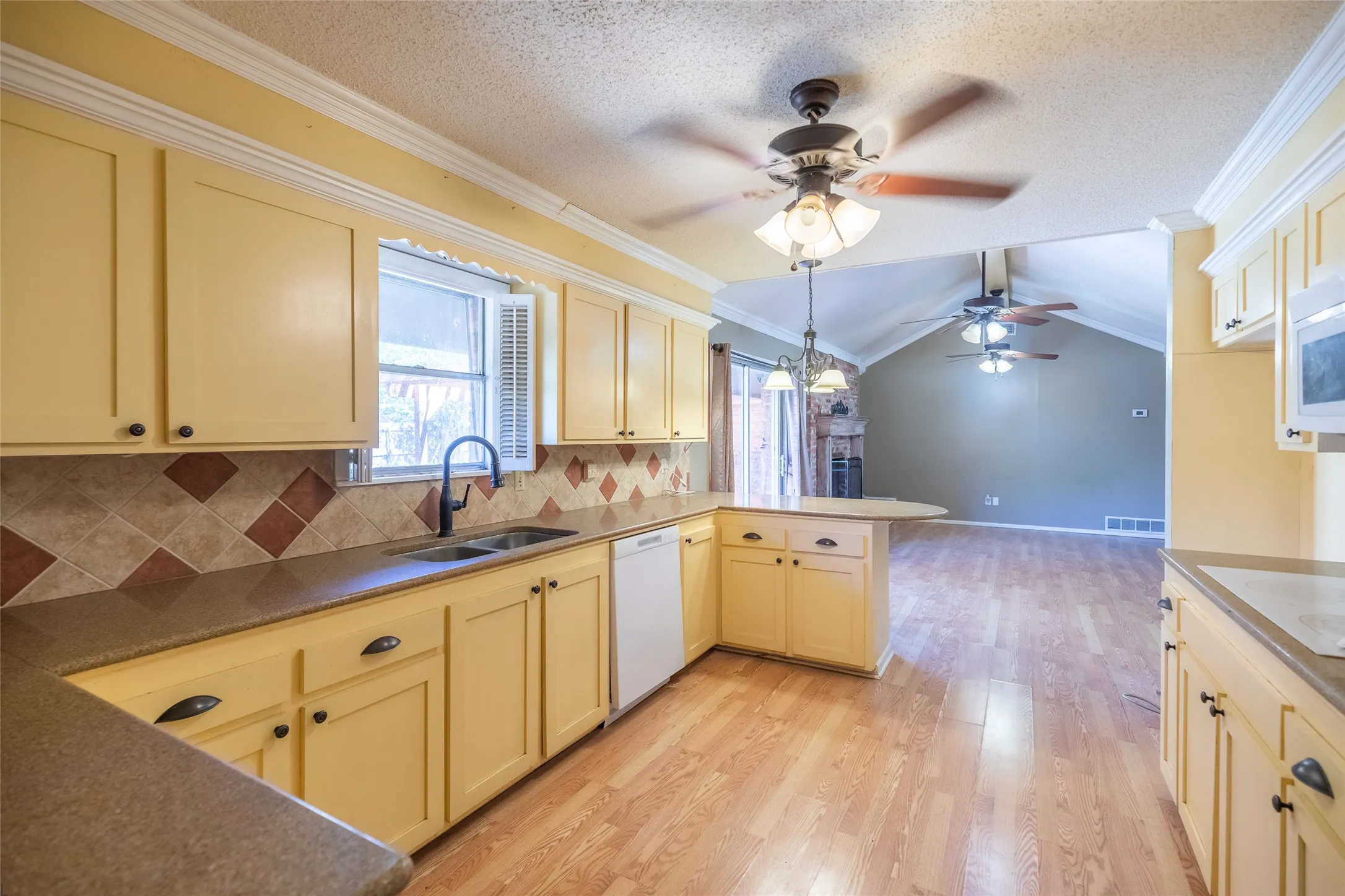 Kitchen featuring abundant cabinetry, dark countertops, a dual basin sink with a gooseneck faucet, a tile backsplash, and wood-finish flooring