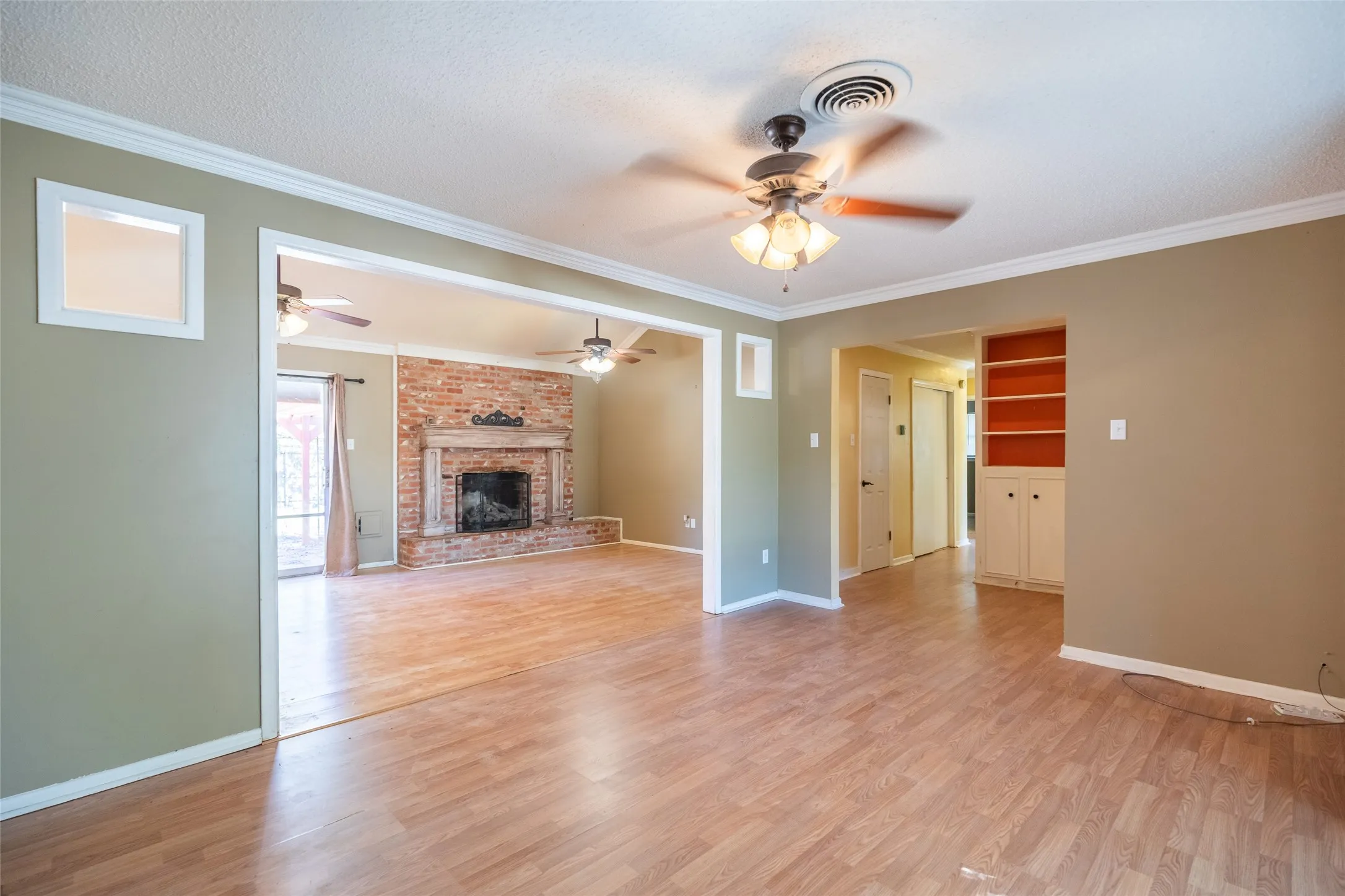Wood-finish flooring throughout, ceiling fan with integrated lighting, built-in shelving, fireplace with brick surround, and white trim