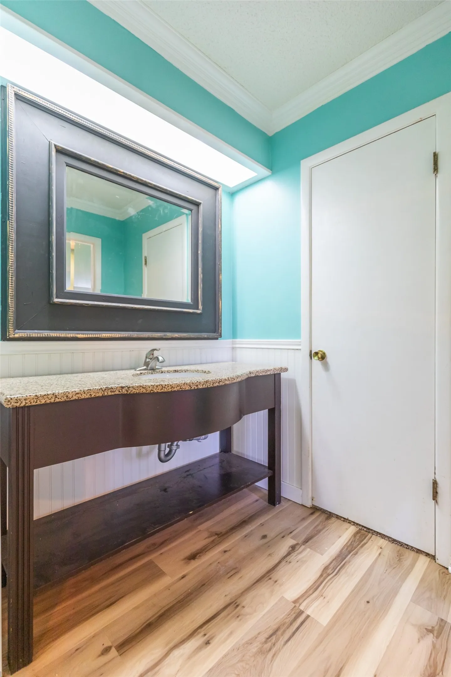 Wood-finish flooring with a vanity featuring a stone-look countertop and an integrated sink
