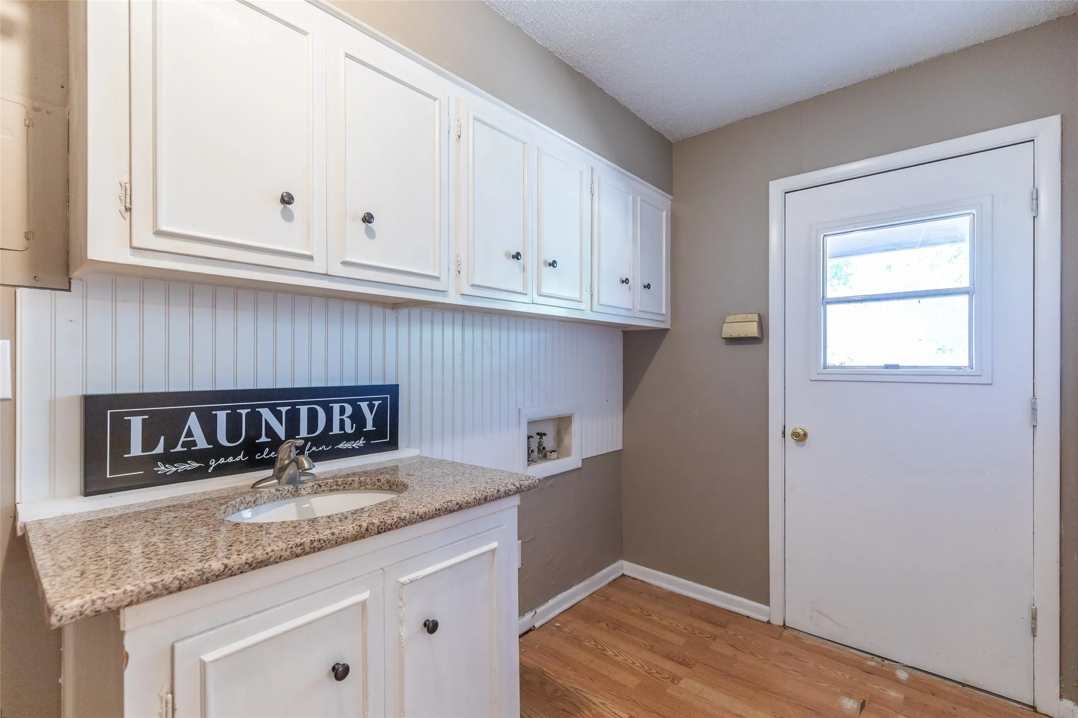 White cabinetry with black hardware, beadboard backsplash, light-toned countertop with integrated sink, and a door with a window pane