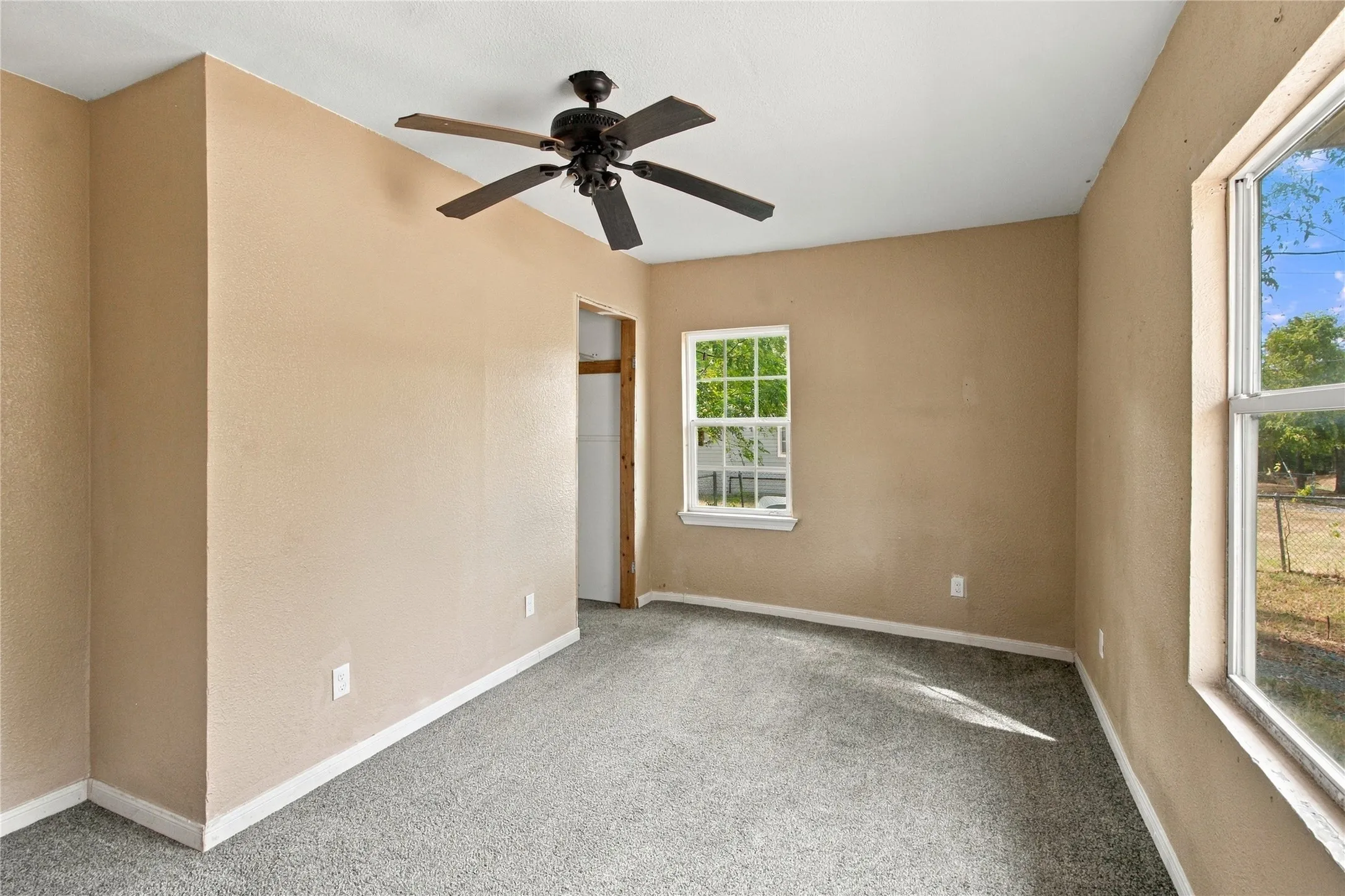 Neutral painted walls, grey carpet flooring, white trim, ceiling fan, and two windows