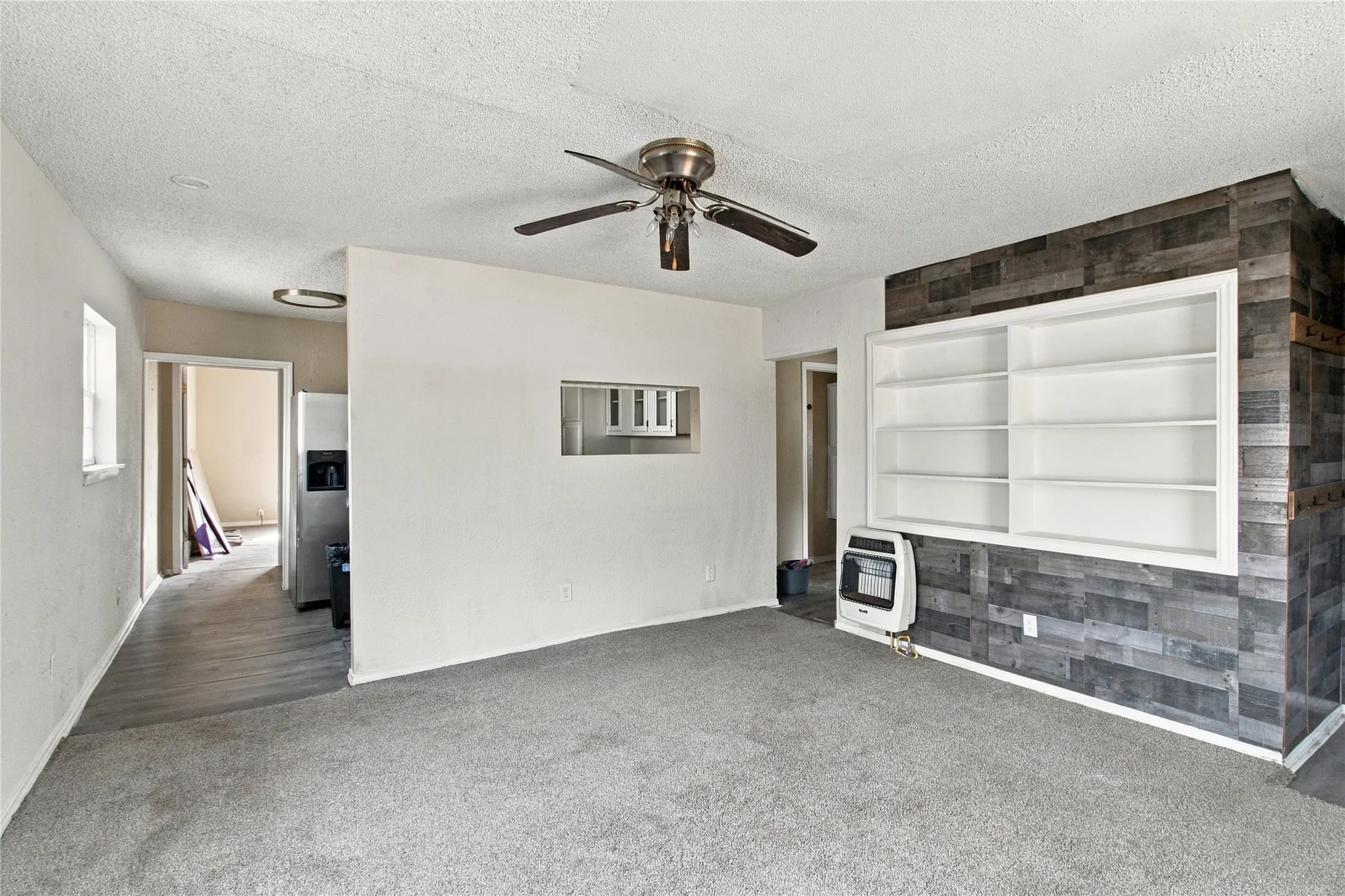 Wall-mounted open shelving with built-in storage, wood panel accent wall, wood-finish flooring, and ceiling fan