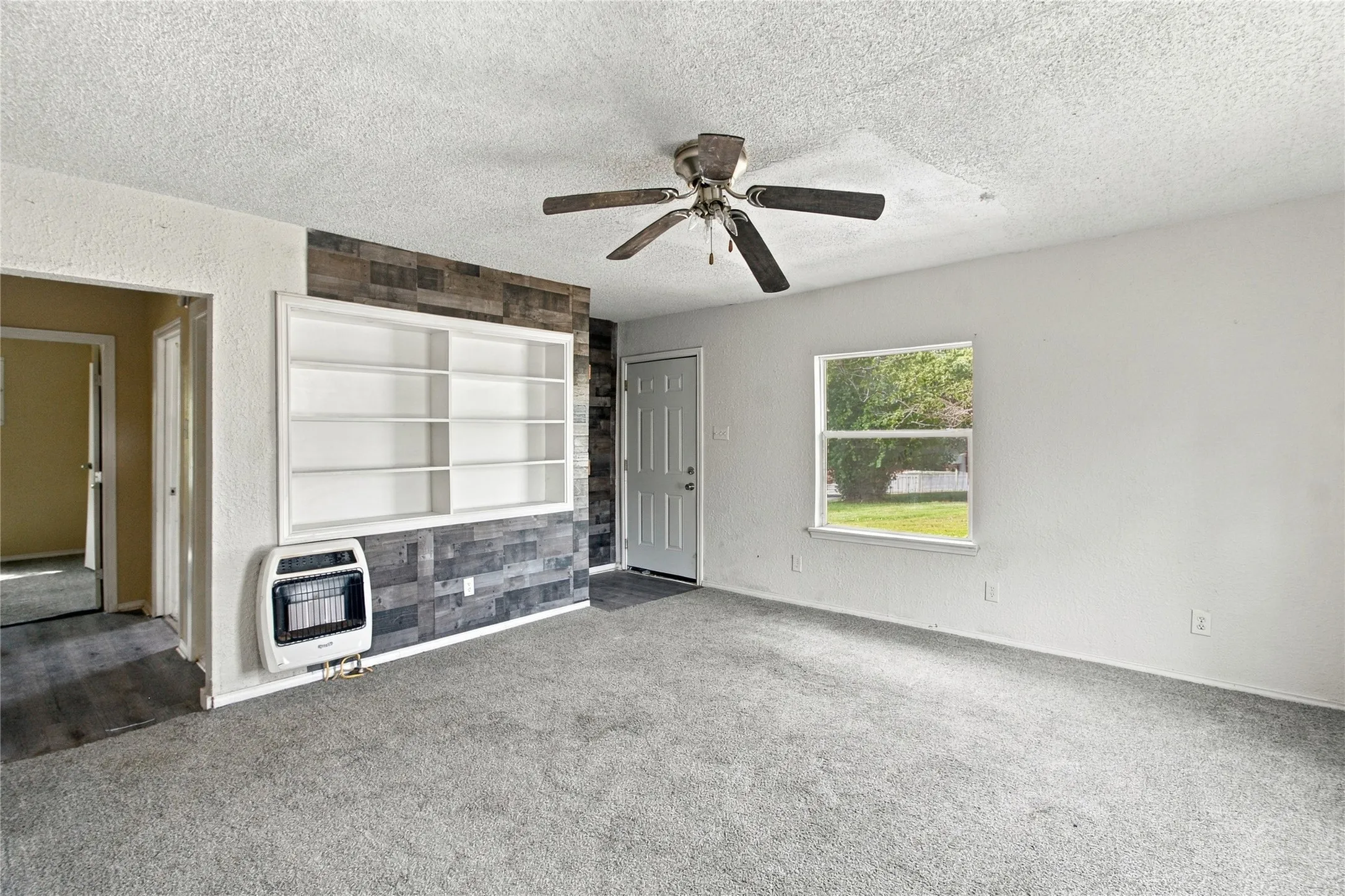 Recessed built-in shelving, wood-look accent wall, ceiling fan, and carpeted flooring