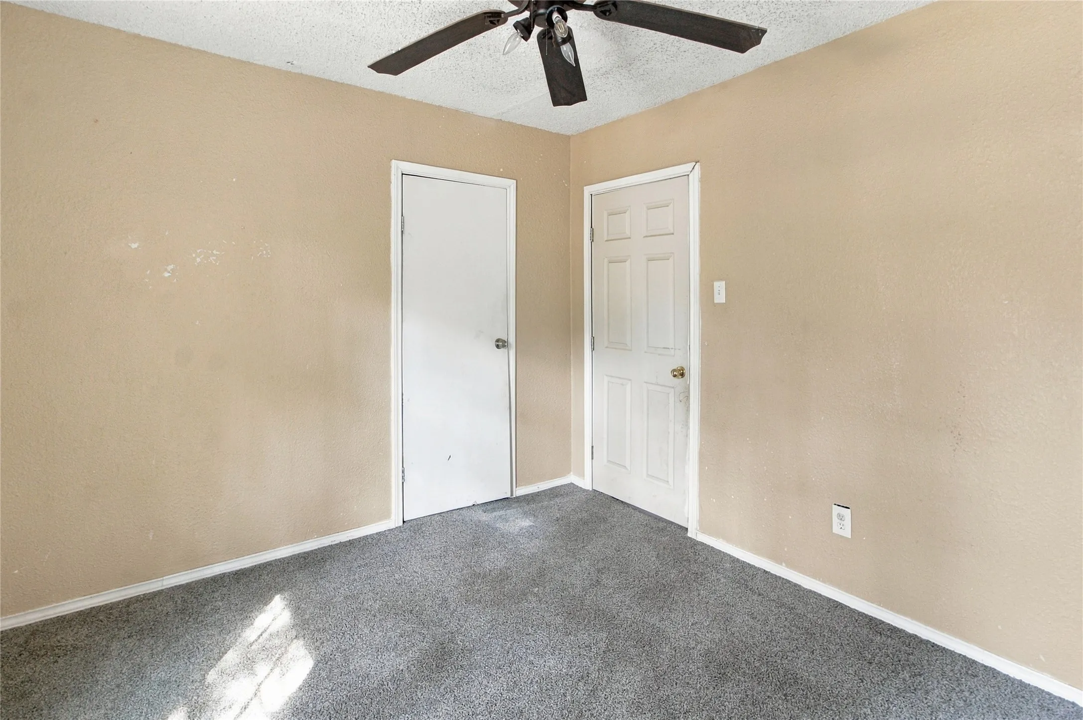 Bright bedroom featuring neutral wall finishes, gray carpet flooring, ceiling fan with integrated lighting, and dual closet access with six-panel doors