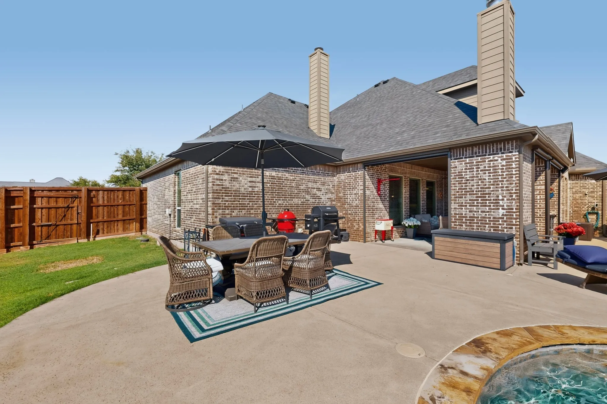 Brick exterior with multiple chimneys, covered patio, concrete patio, and fenced yard