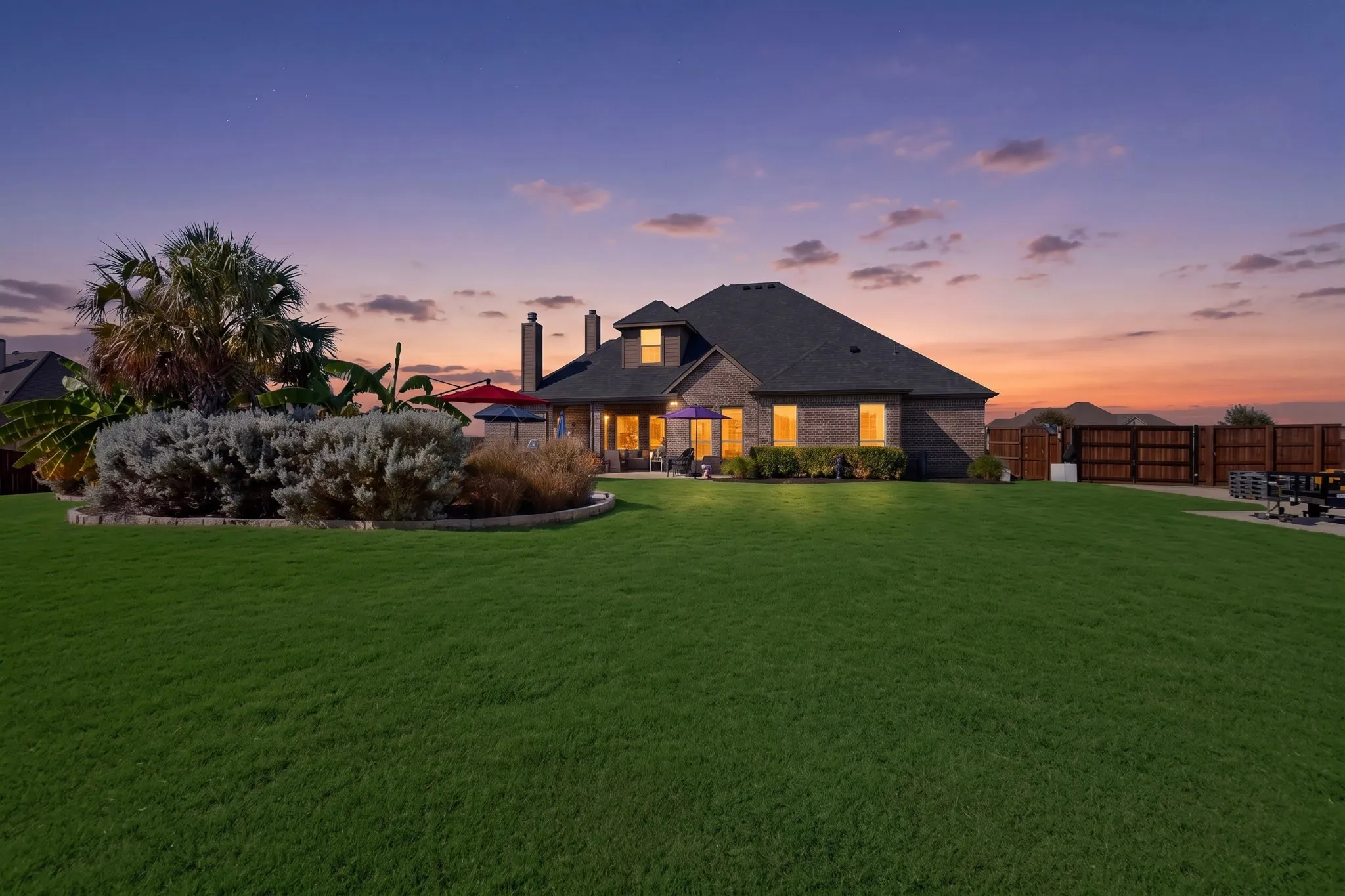 Elegant brick residence with hipped roofline and illuminated interior showcasing multiple windows