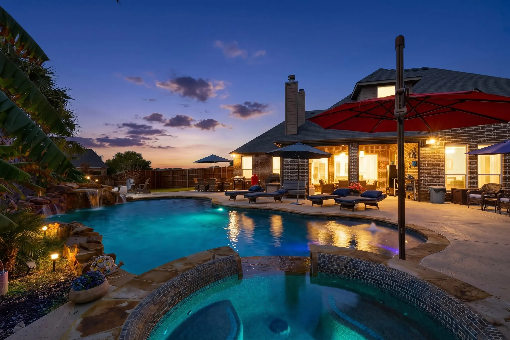 Custom-shaped swimming pool with an integrated spa, rock waterfall feature, and surrounding concrete patio
