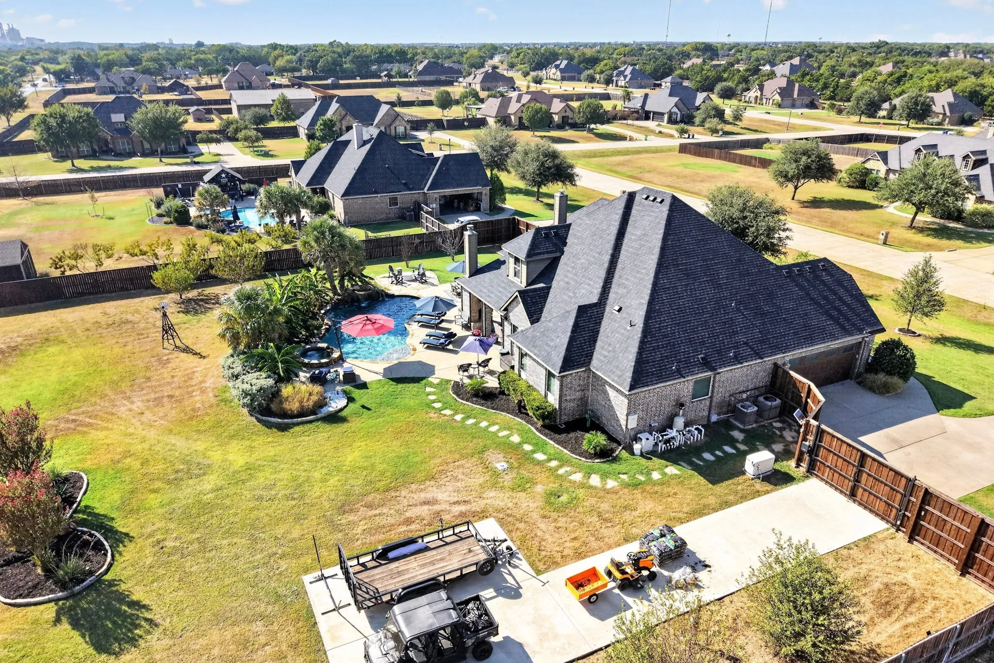 Brick exterior property with multi-peak roofline, concrete driveway, and privacy fencing