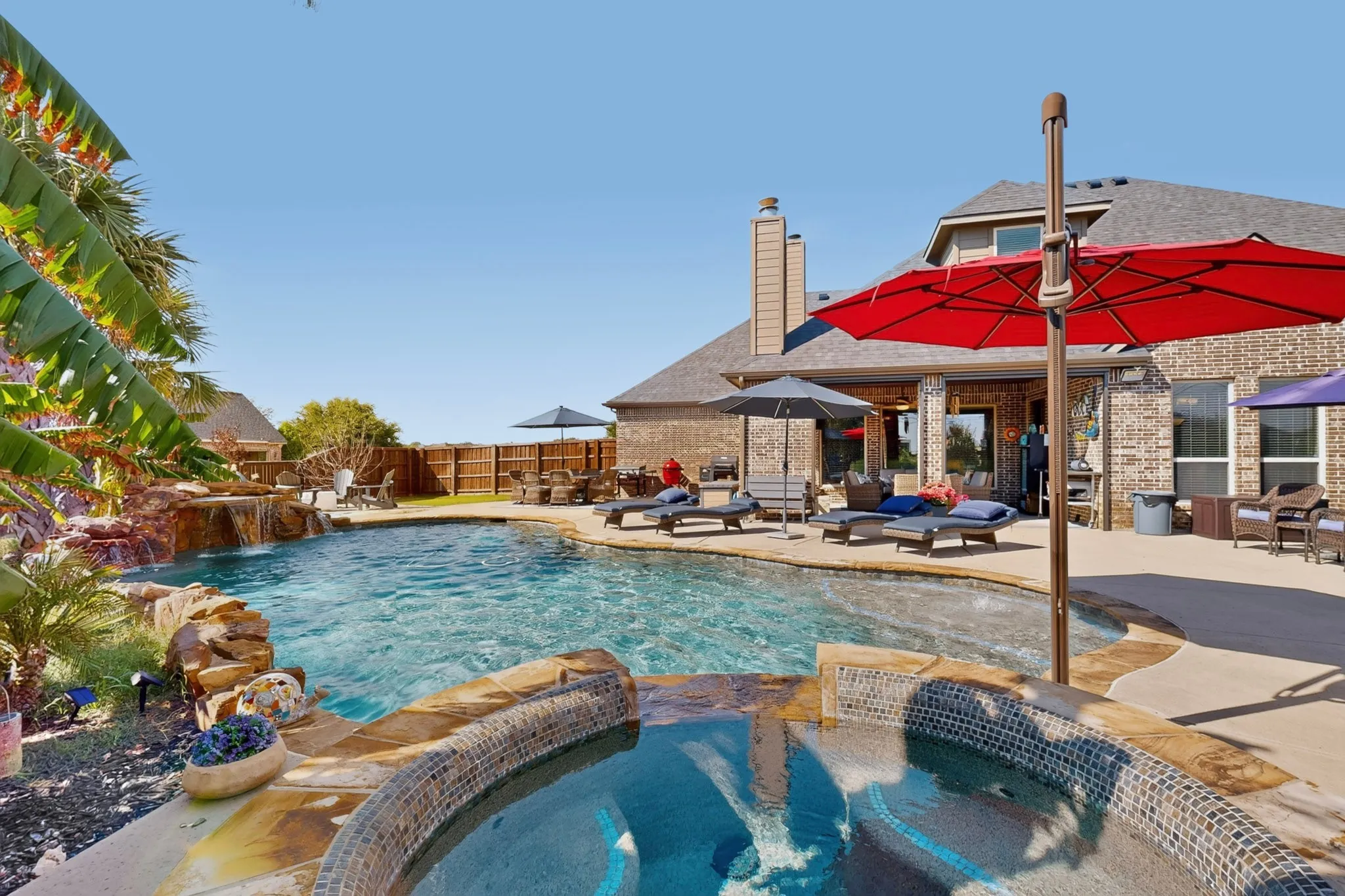 Lagoon-style swimming pool with rock waterfall feature, integrated spa with mosaic tile, and extensive concrete patio