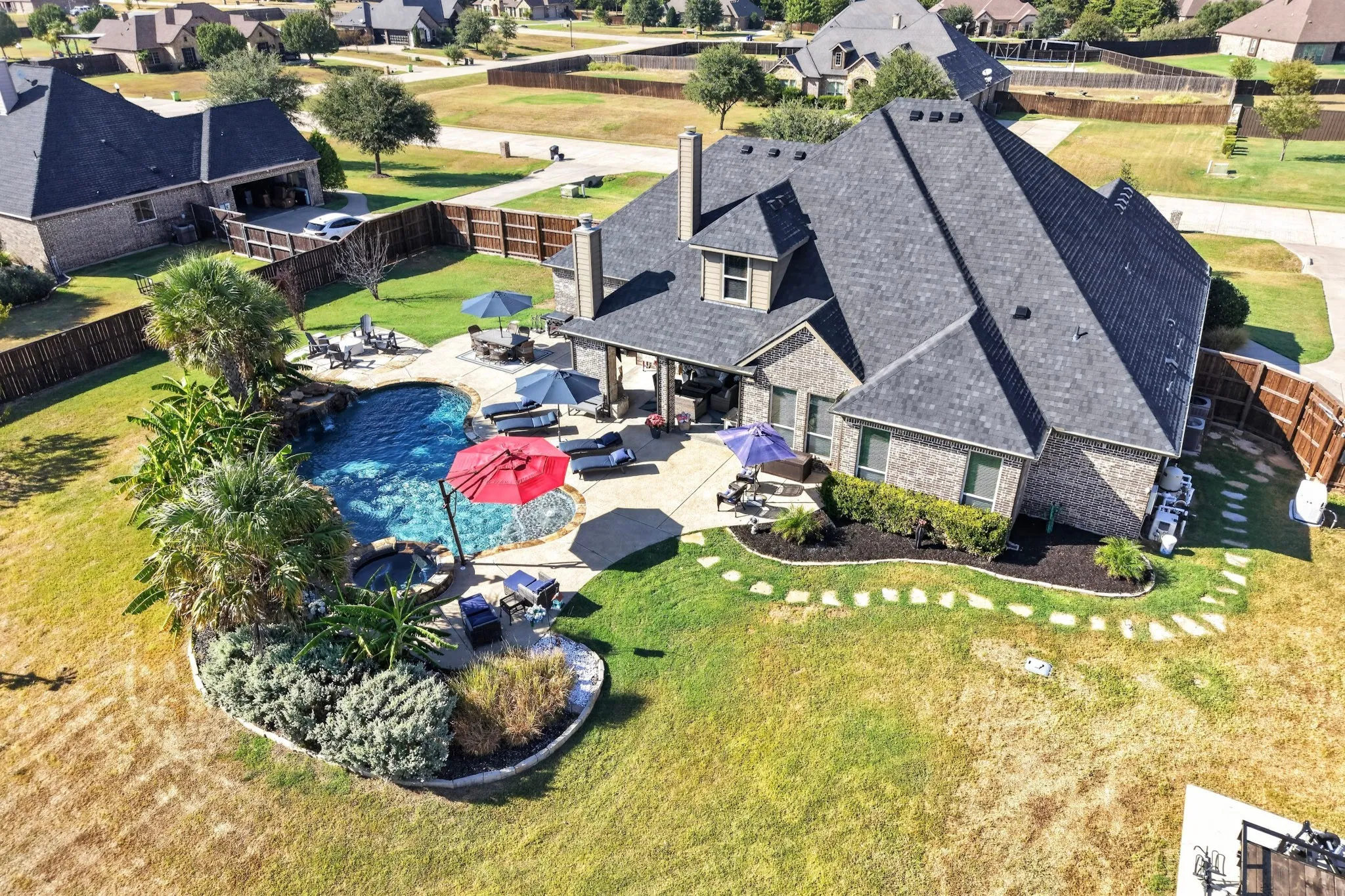 Brick exterior residence with a multi-level roofline, featuring an in-ground swimming pool, an integrated spa, and a stone patio