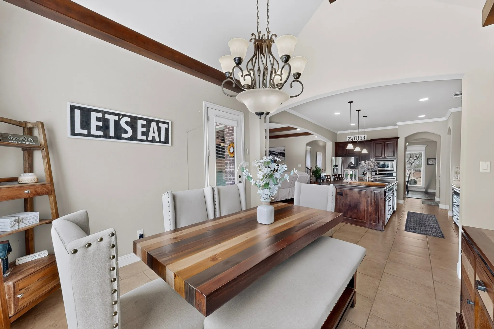 Tray ceiling with exposed wood-finish beams, arched doorways, tile flooring, and recessed lighting