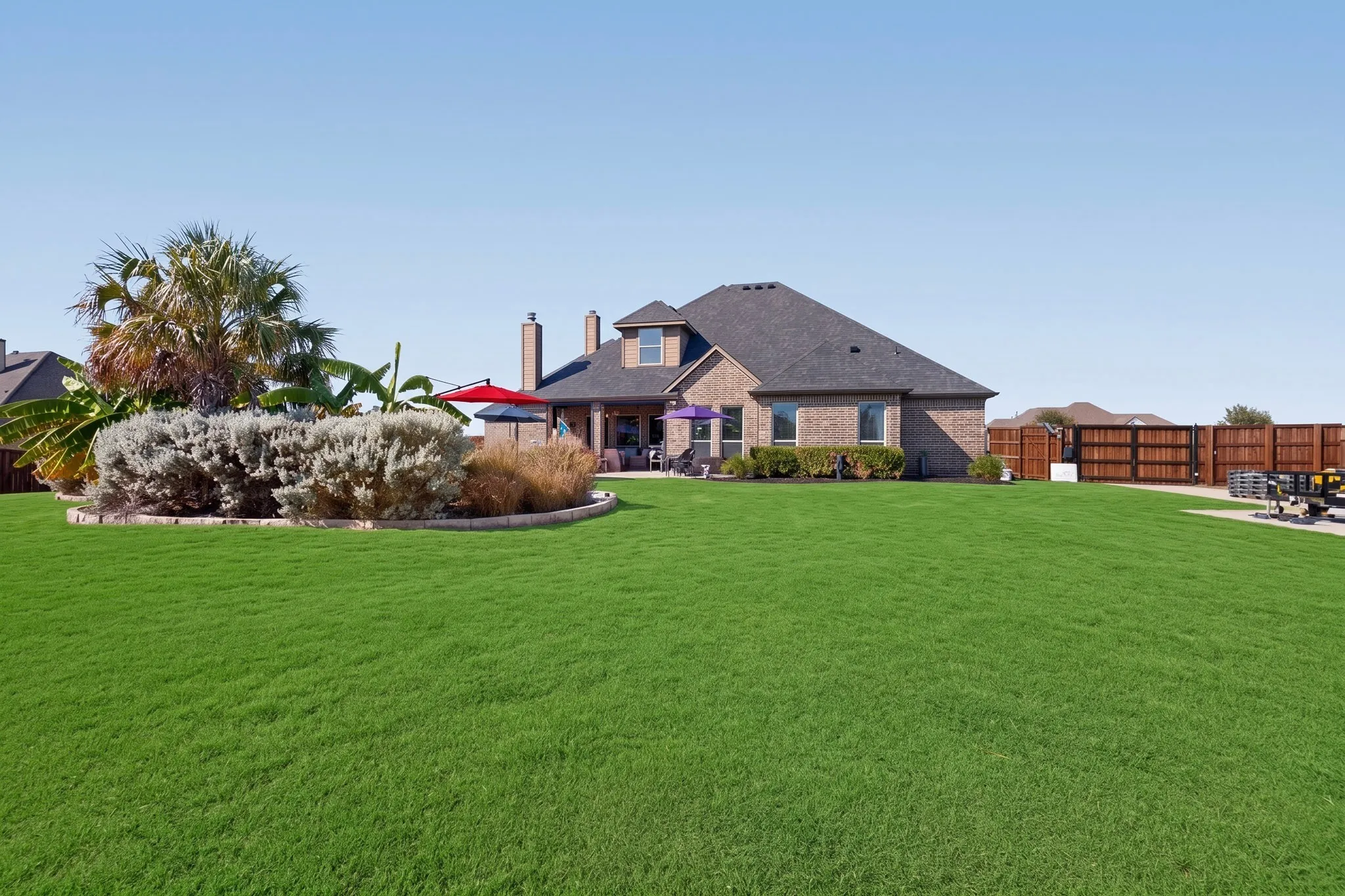 Expansive green lawn, brick exterior, dark-toned roof, paved patio, and wood privacy fencing