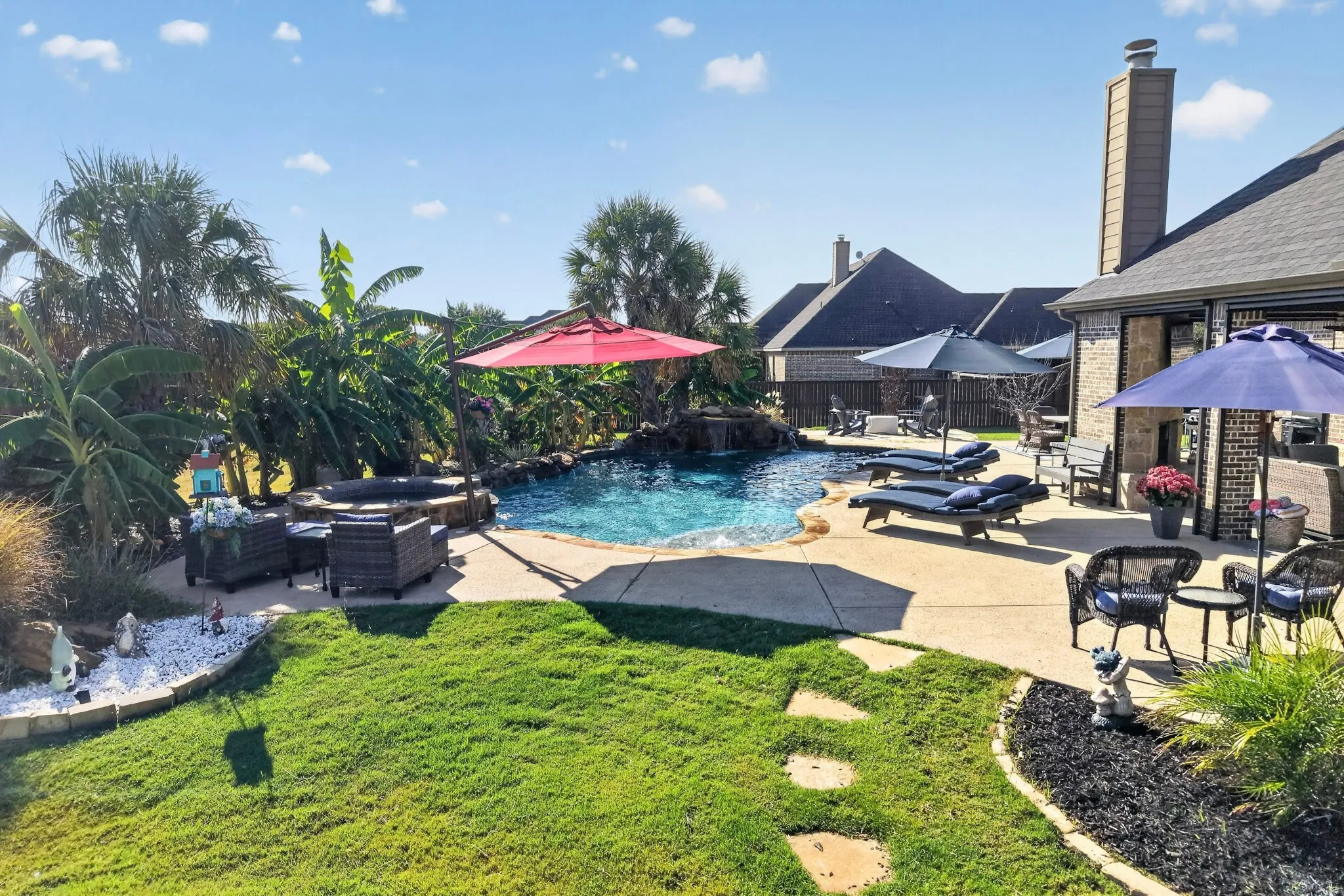 Landscaped backyard featuring a freeform swimming pool with a rock waterfall and integrated spa