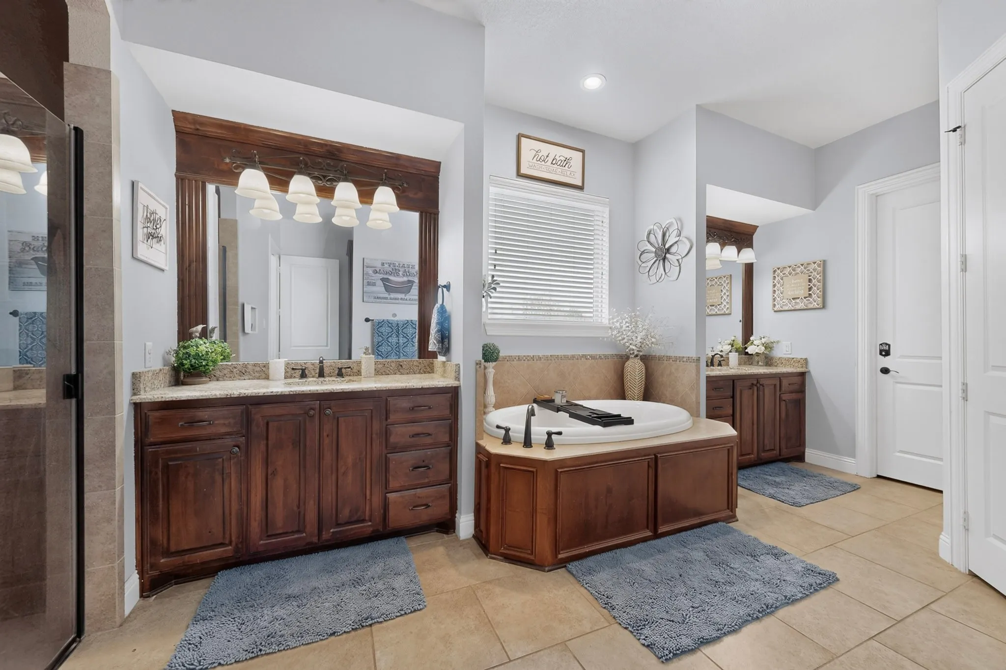 Dual wood-finish vanities with stone countertops, a built-in soaking tub, and a separate glass-enclosed shower